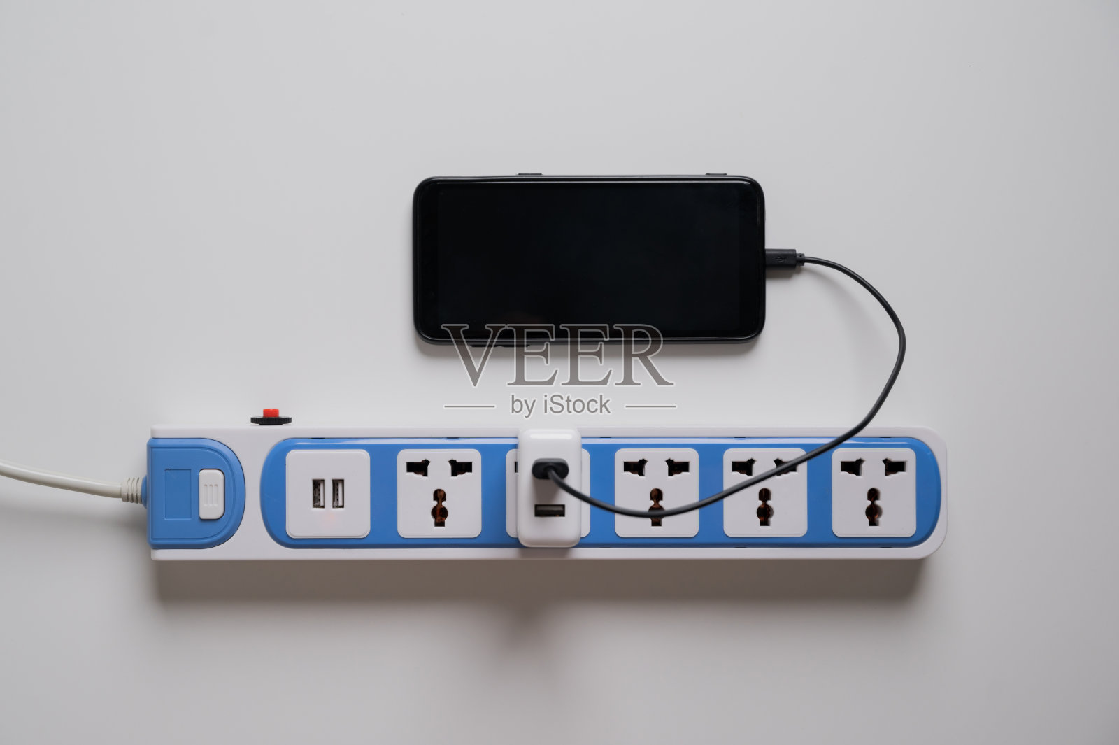 这款智能手机在白色桌子上的一个电源插板上充电。房子里的电气设备、电线和电源线。照片摄影图片