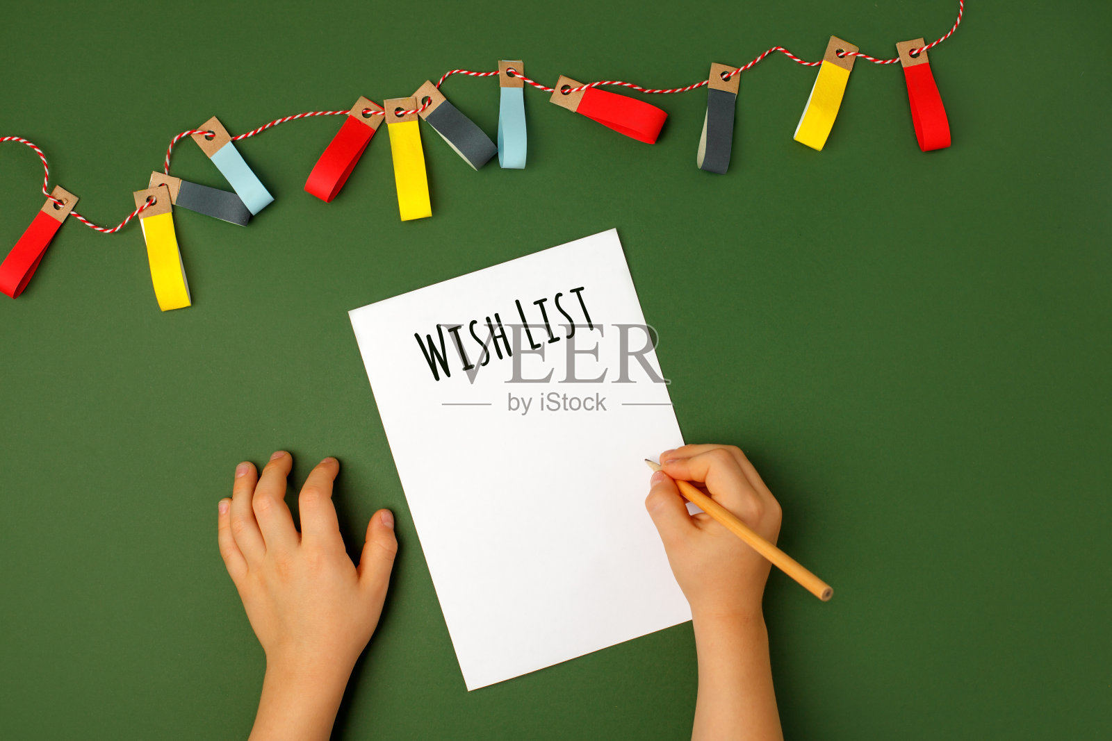 冬天的假期。Top view of kid hands at Christmas making Christmas presents wish list on natural shades of green background, Christmas, New Year decoration, copy space .圣诞老人在圣诞节制作圣诞礼物的愿望清单照片摄影图片