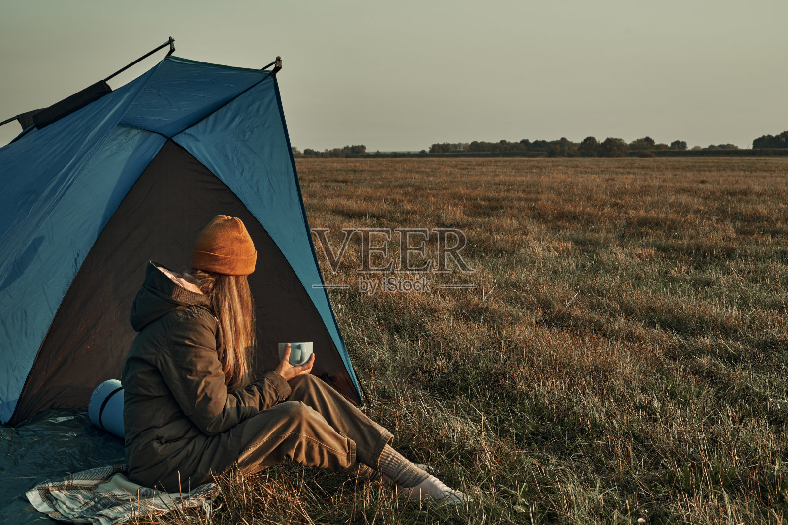 一个女孩坐在帐篷里，迎接寒冷的黎明。旅行。照片摄影图片