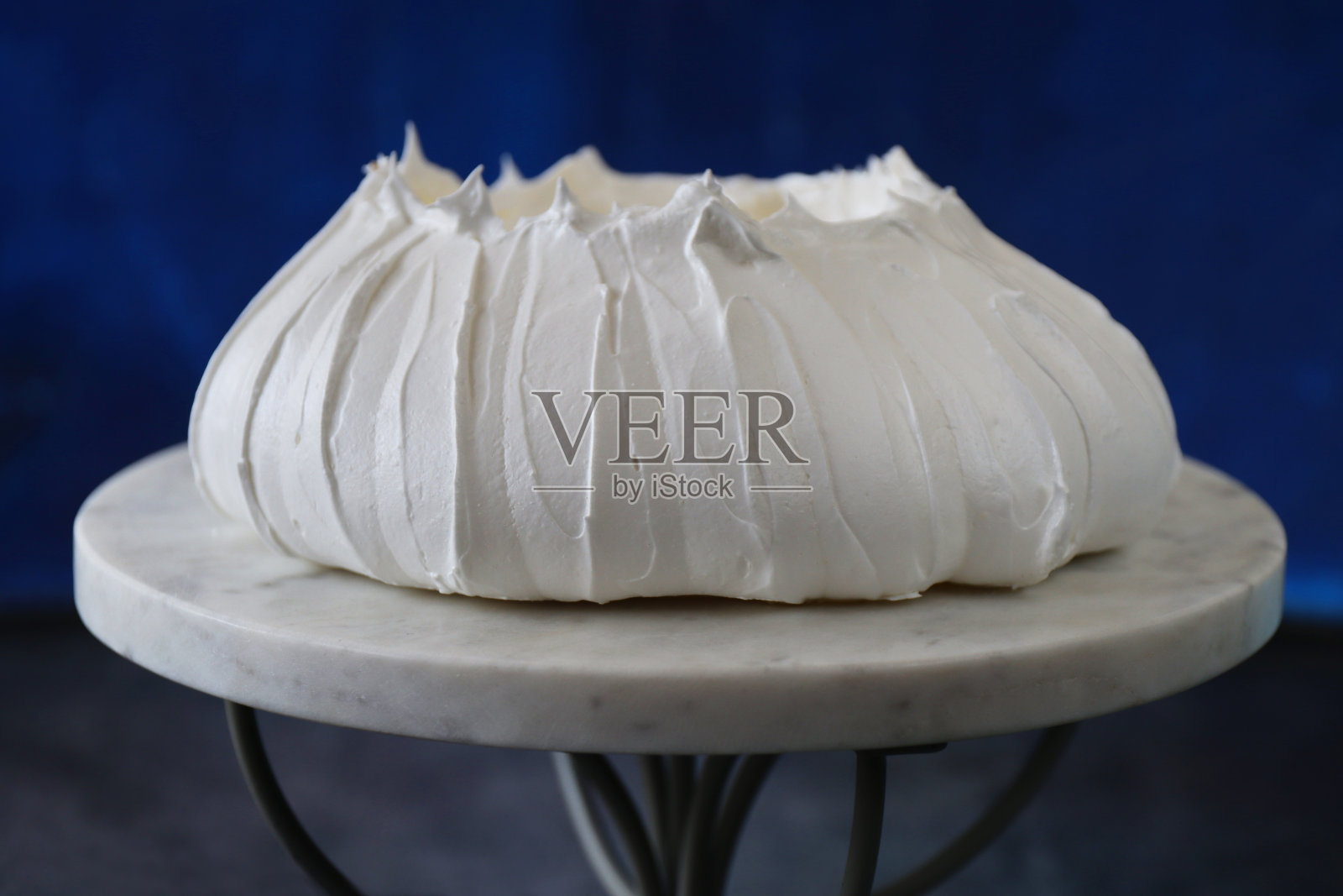 在蓝色背景下，大理石和金属蛋糕架上的新鲜空心蛋白酥皮特写，聚焦前景照片摄影图片