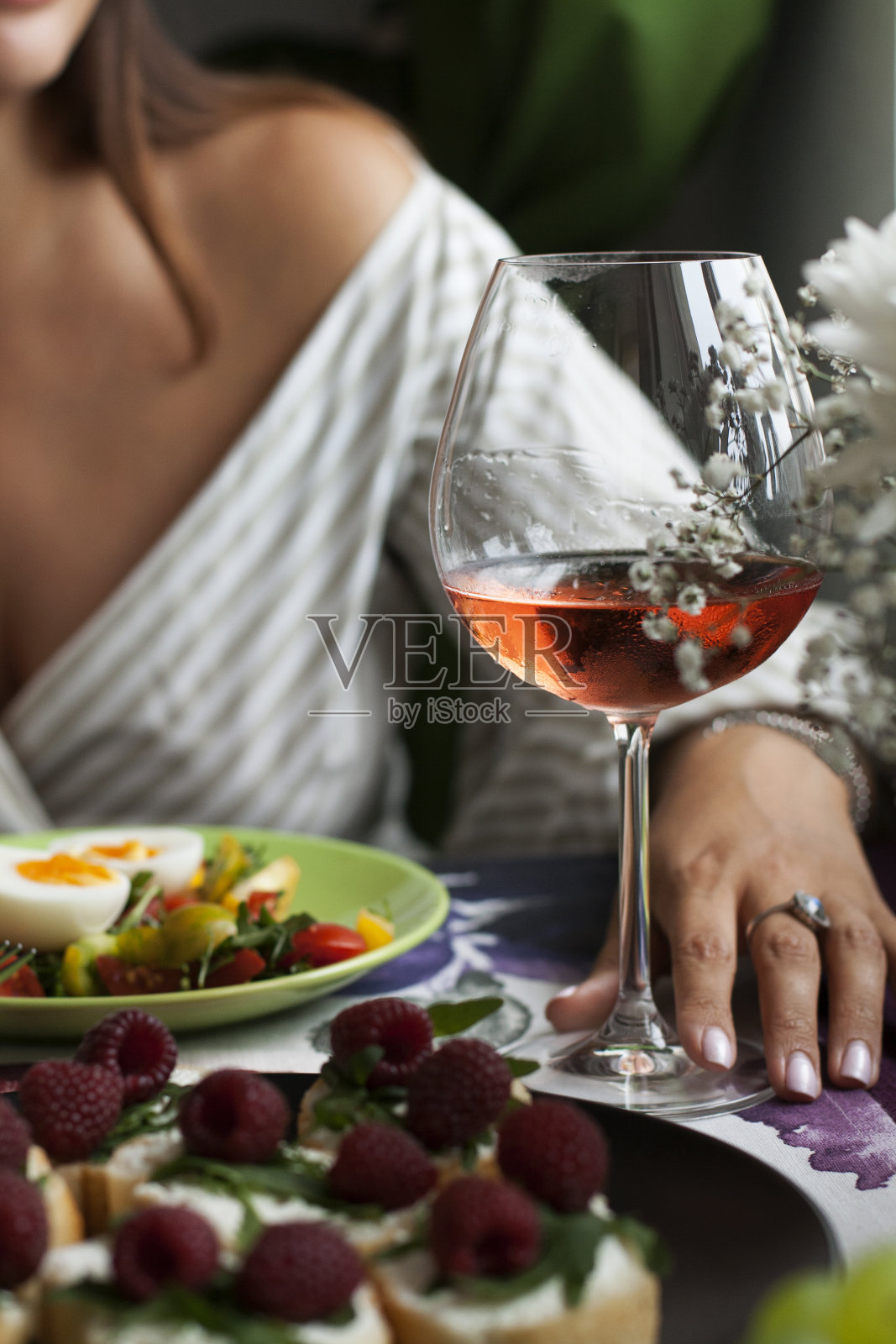 在餐厅享用一顿美味的双人晚餐:一盘煮鸡蛋的新鲜蔬菜沙拉，一盘带芝麻菜和覆盆子香味的法棍面包片，一盘马苏里拉奶酪和橄榄点心，一串多汁的葡萄和一杯葡萄酒。照片摄影图片