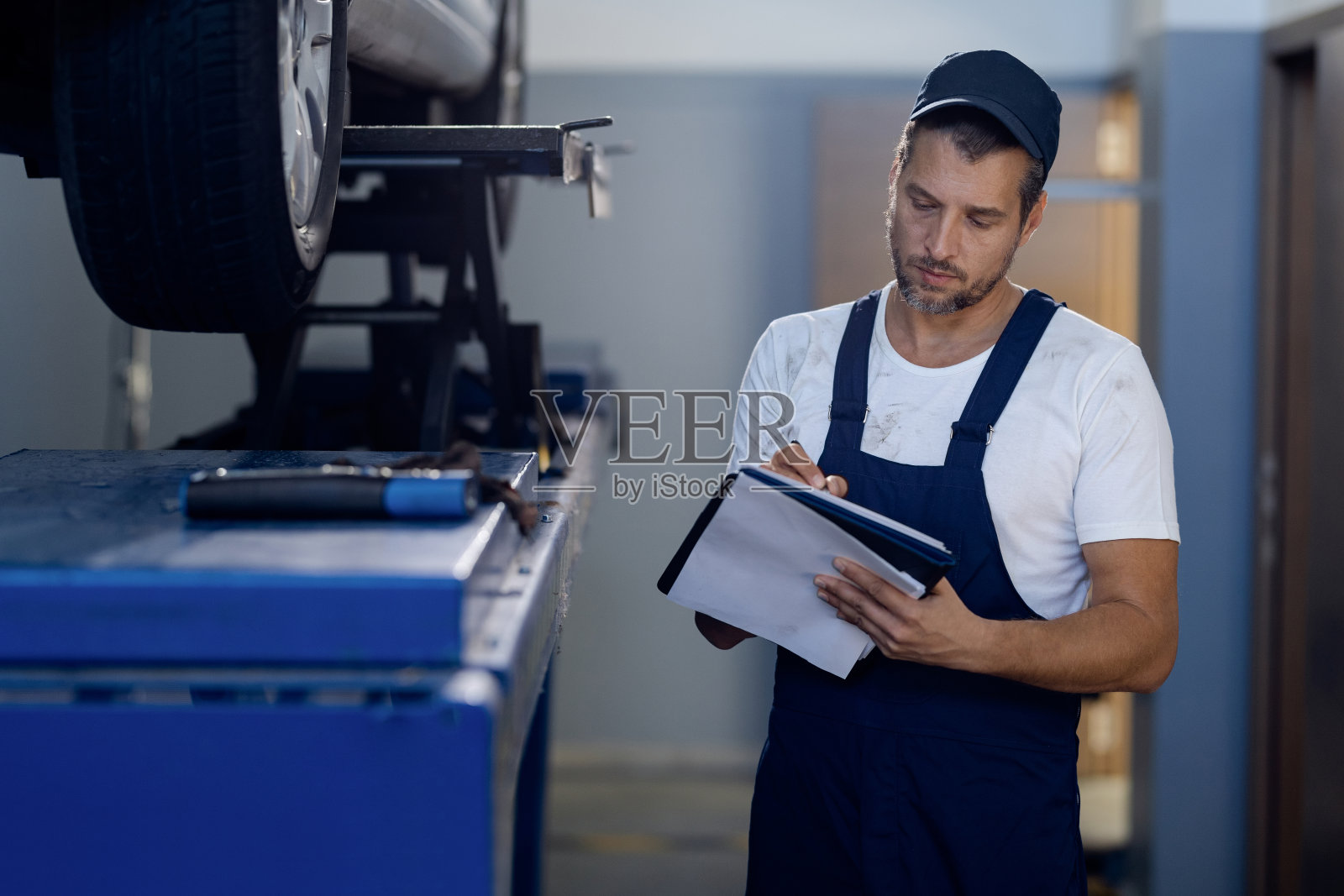 汽车修理工在车间检查汽车时写笔记。照片摄影图片
