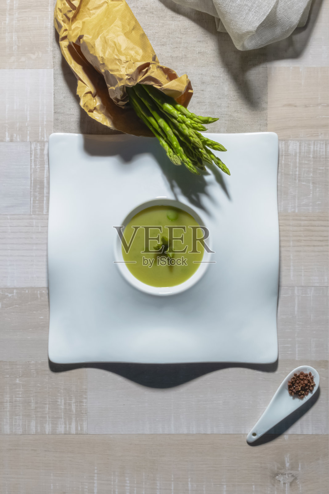 这是一道美味的蔬菜汤，里面有芦笋，还有一个装着新鲜芦笋的纸袋和一个装着蔬菜种子的小盘子。健康和素食的理念。照片摄影图片