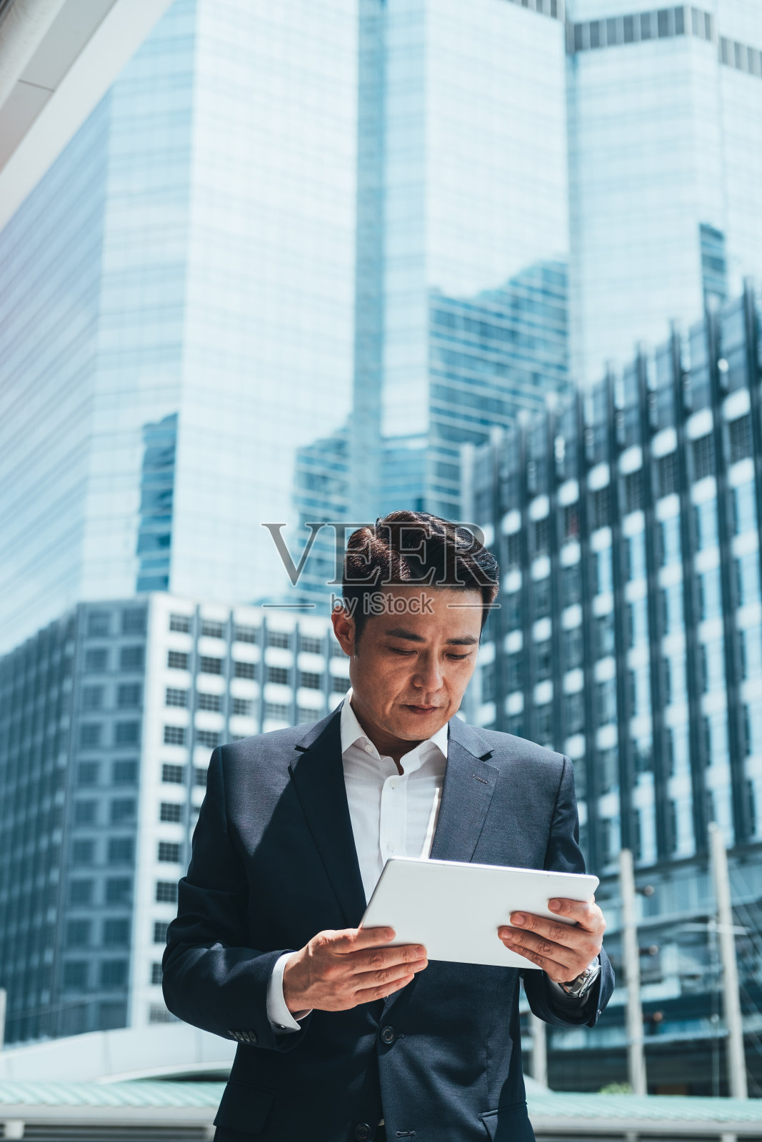 英俊的商人在城市户外使用平板电脑，以办公大楼为背景照片摄影图片