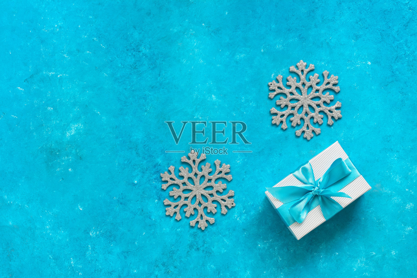 礼物与蓝色丝带和雪花在绿松石垃圾背景。圣诞组成。俯视图，平放，复制空间。照片摄影图片