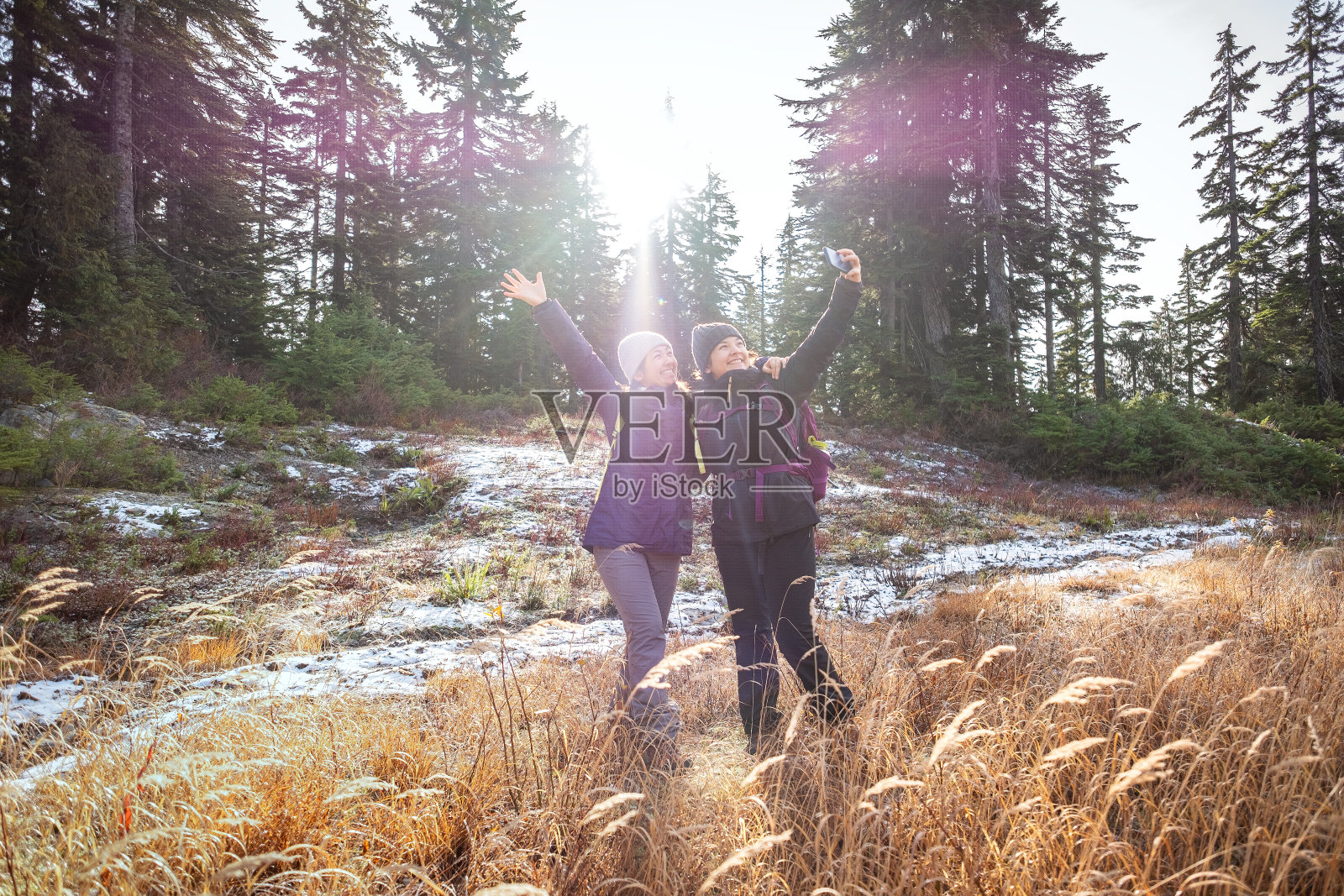 冬季徒步旅行，多民族姐妹在雪道上用智能手机自拍照片摄影图片