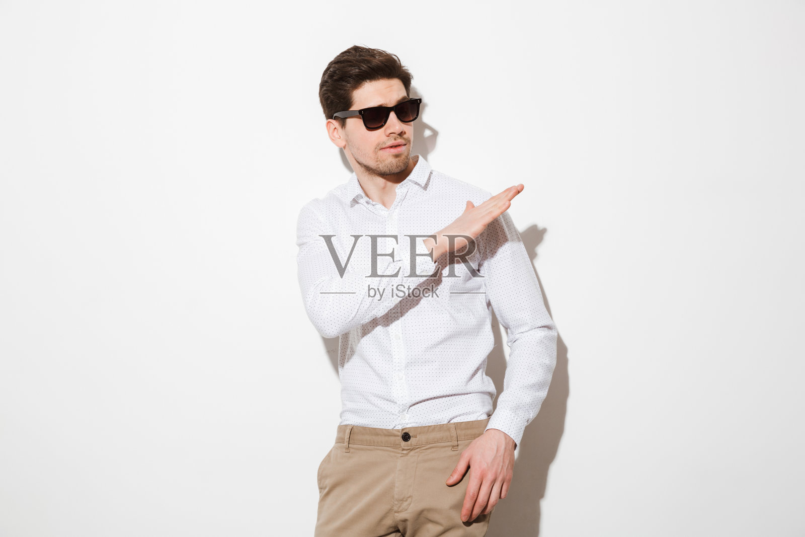 白人时尚男子的肖像穿着衬衫和黑色太阳镜手势，而看一边，在白色的背景与阴影照片摄影图片