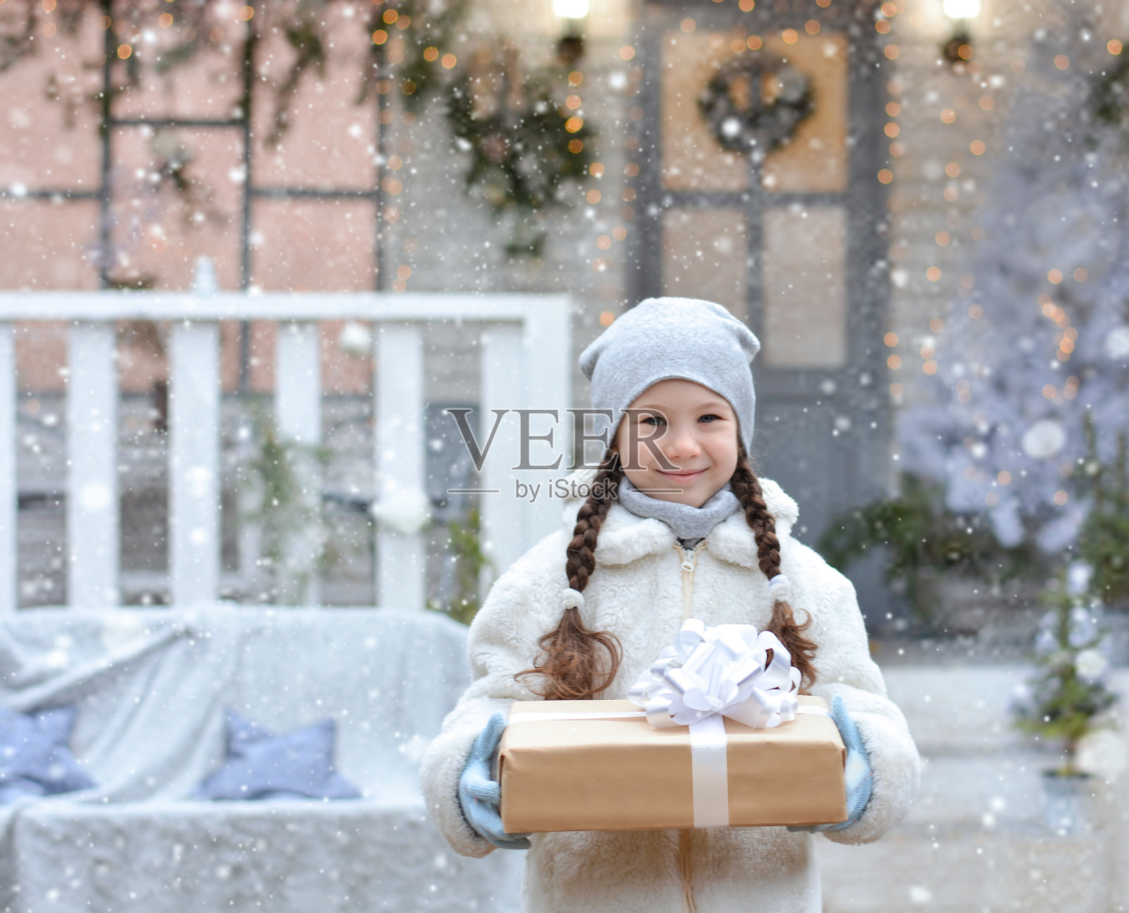 快乐的小女孩拿着一个礼物盒在圣诞房子的背景!新年快乐，圣诞快乐!照片摄影图片