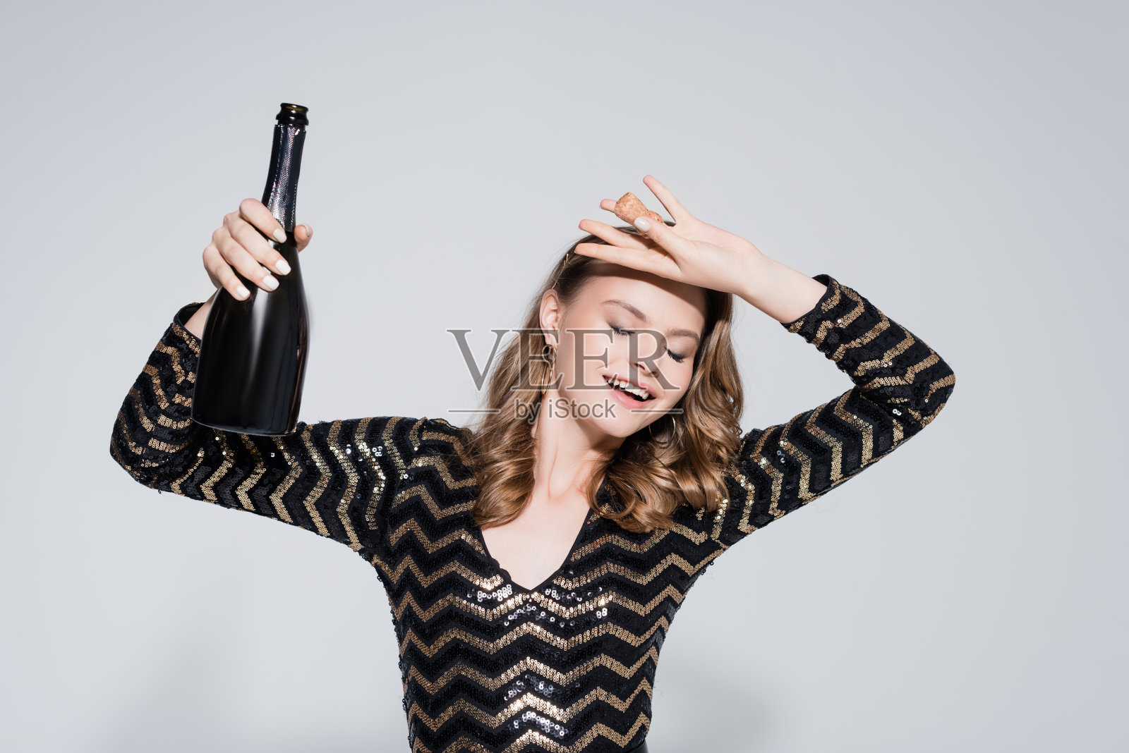 快乐的女人拿着一瓶香槟在灰色照片摄影图片