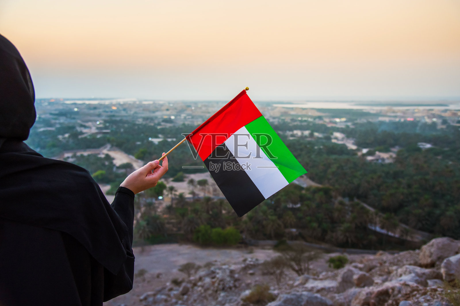 日落时分在沙漠山中手持阿联酋国旗的阿联酋女性照片摄影图片