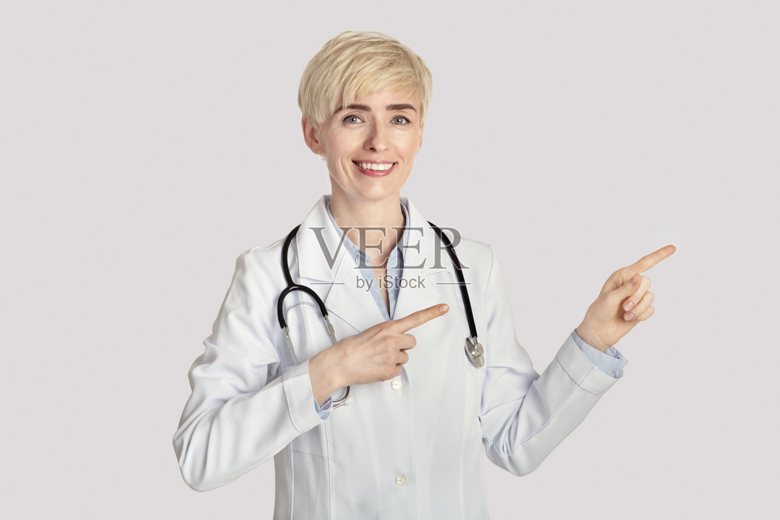 微笑的中年女医生在白大褂与听诊器指向空照片摄影图片