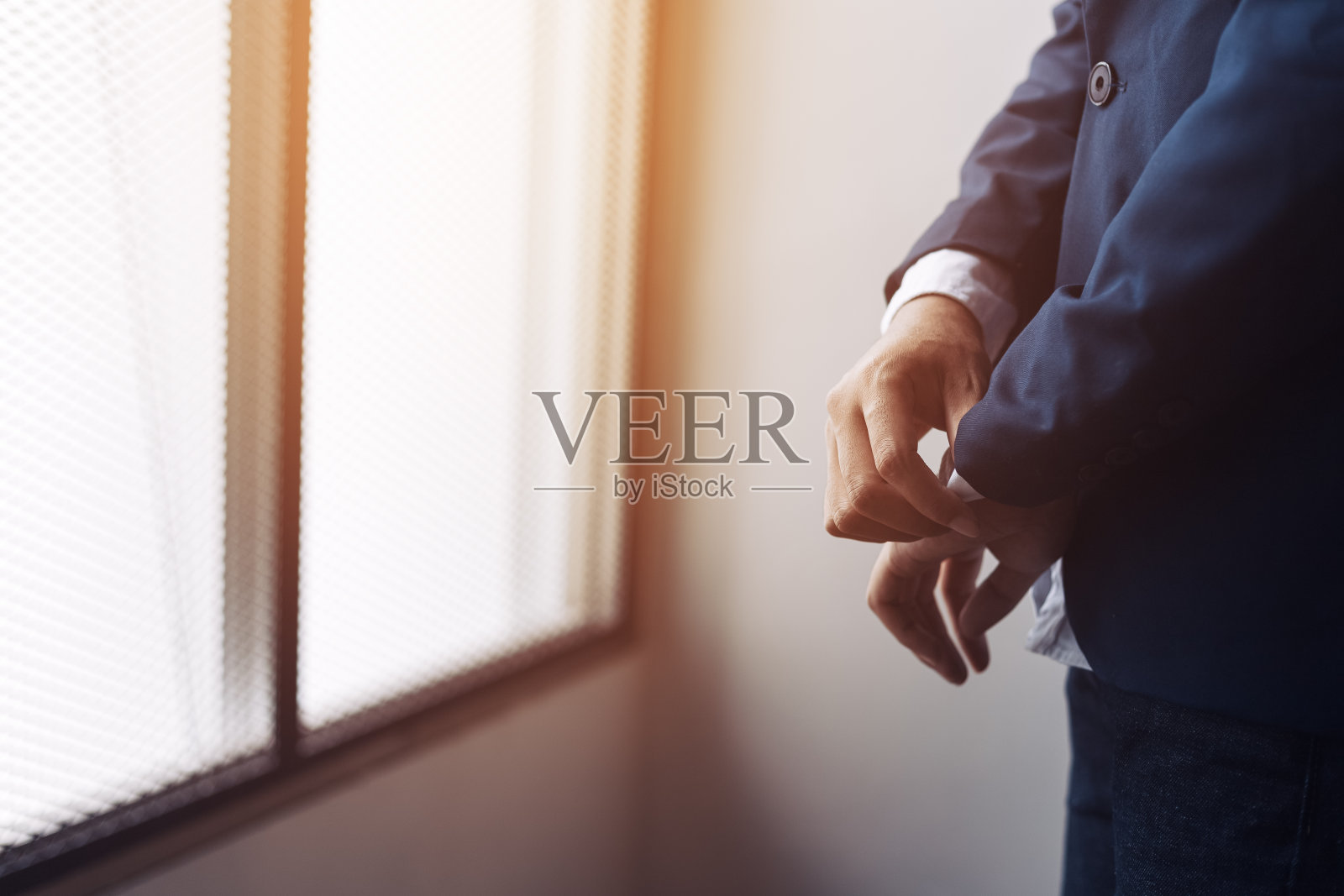 穿着西装的商人把袖扣或纽扣系在经典的外套和工厂背景上。照片摄影图片