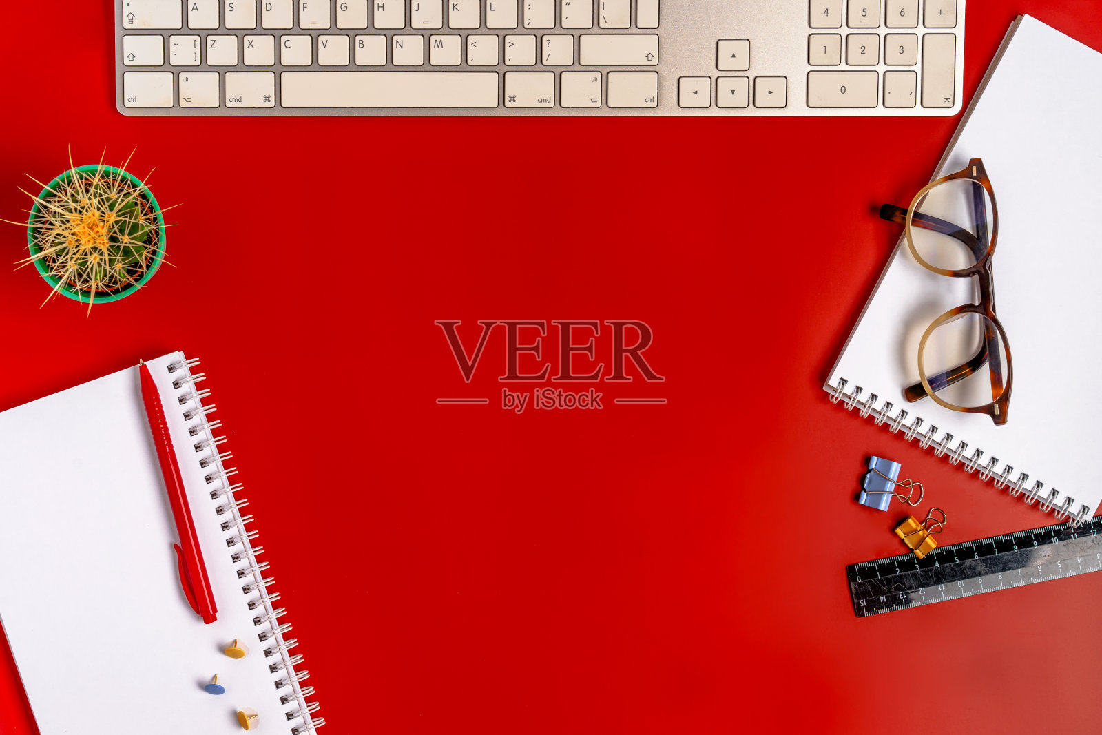 俯视图的办公桌。红色背景上有一个空笔记本、键盘、文具和咖啡杯的工作空间。照片摄影图片