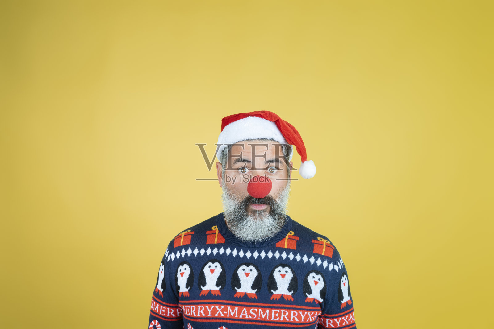 一个男人的肖像在圣诞老人的帽子与红色小丑鼻子在黄色的背景照片摄影图片