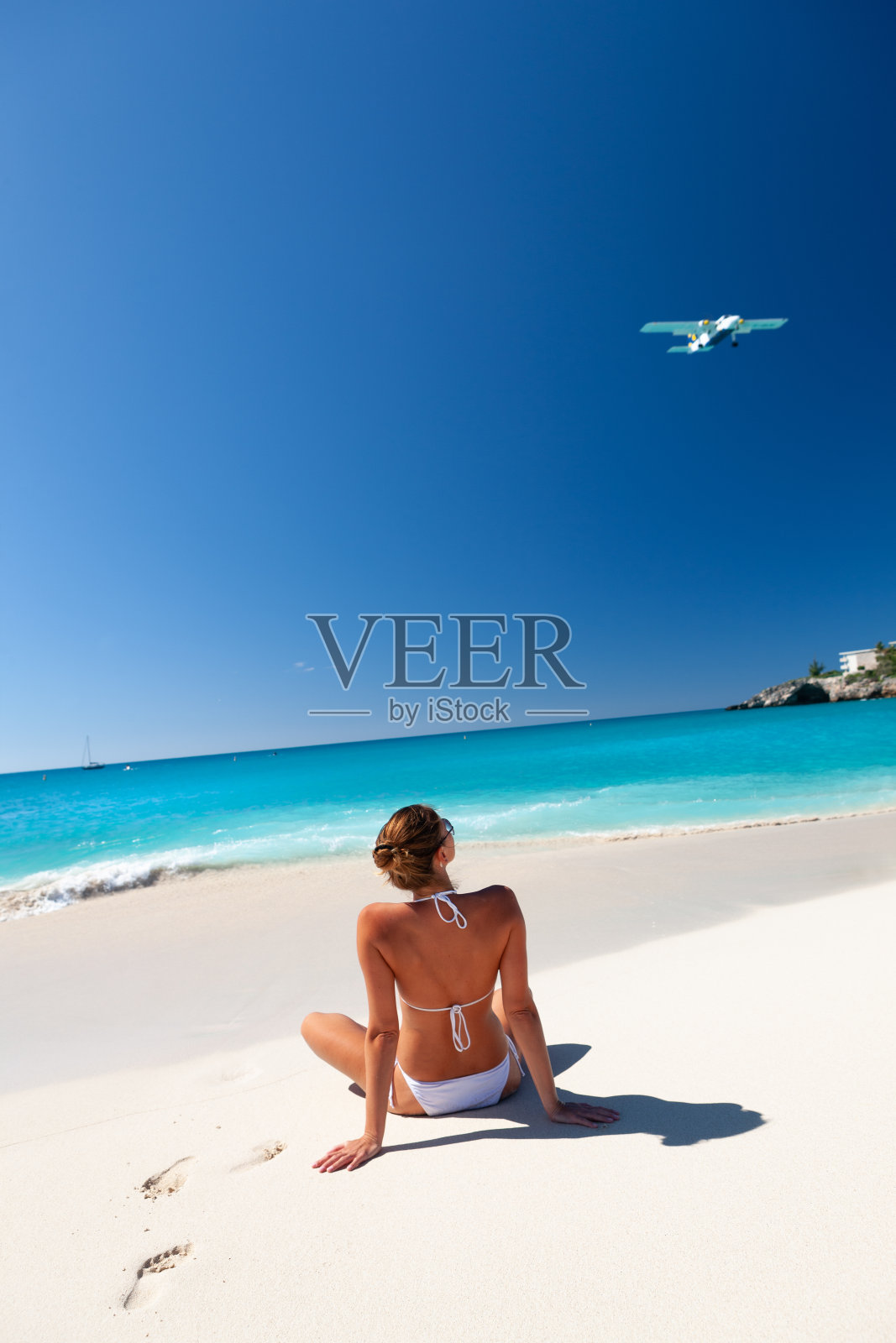 女人在热带海滩的海岸线上放松，飞机飞过照片摄影图片