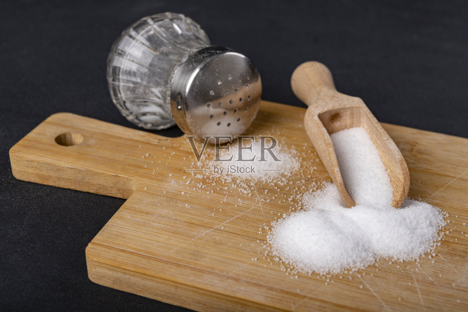 一个装满白色食盐的木勺。在家庭烹饪中添加到菜肴中的调味剂。黑暗的背景。照片摄影图片