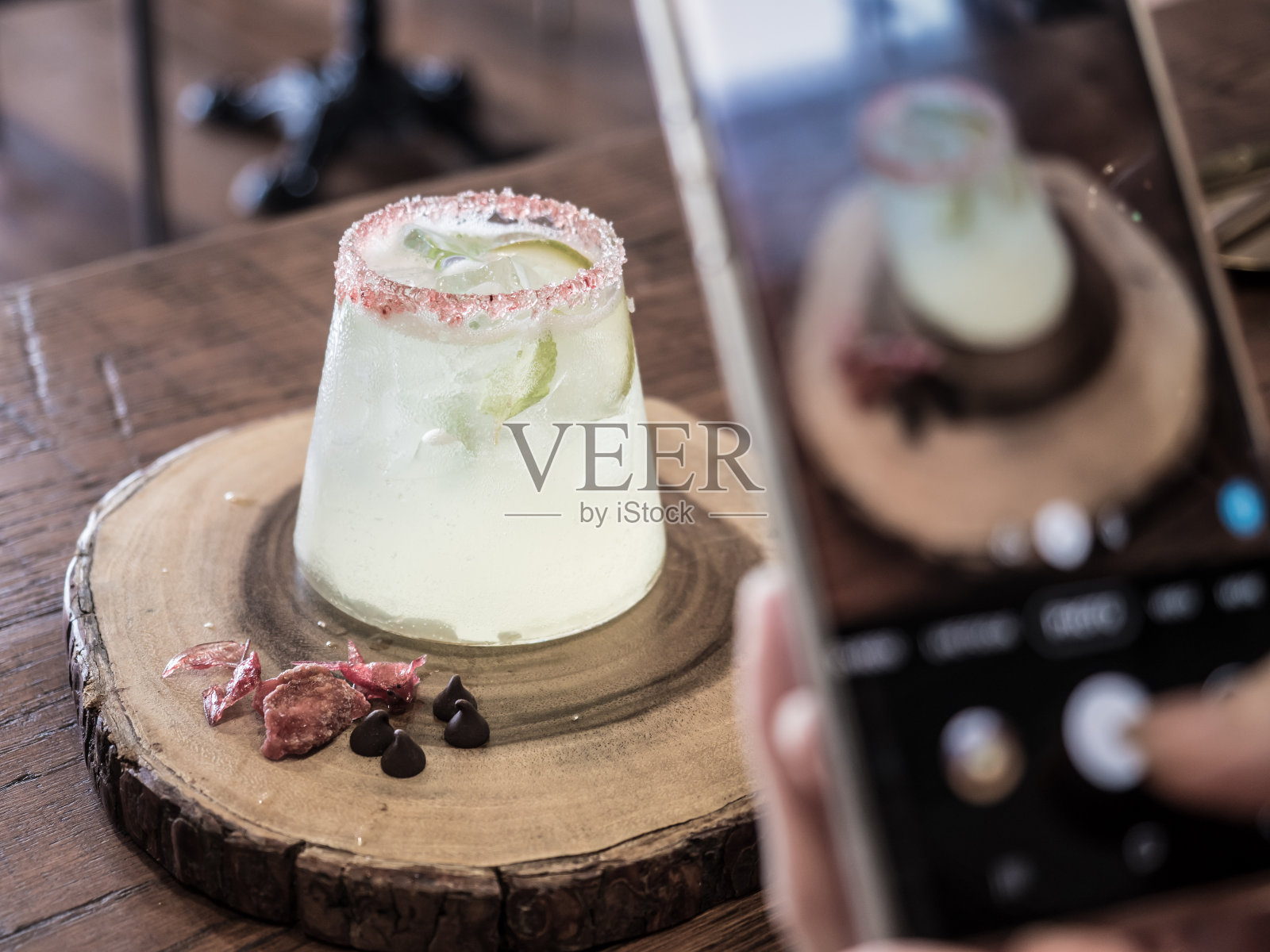 使用智能手机拍照的人，当服务。漂亮的鸡尾酒装饰在木桌上。为社交网络拍照。照片摄影图片