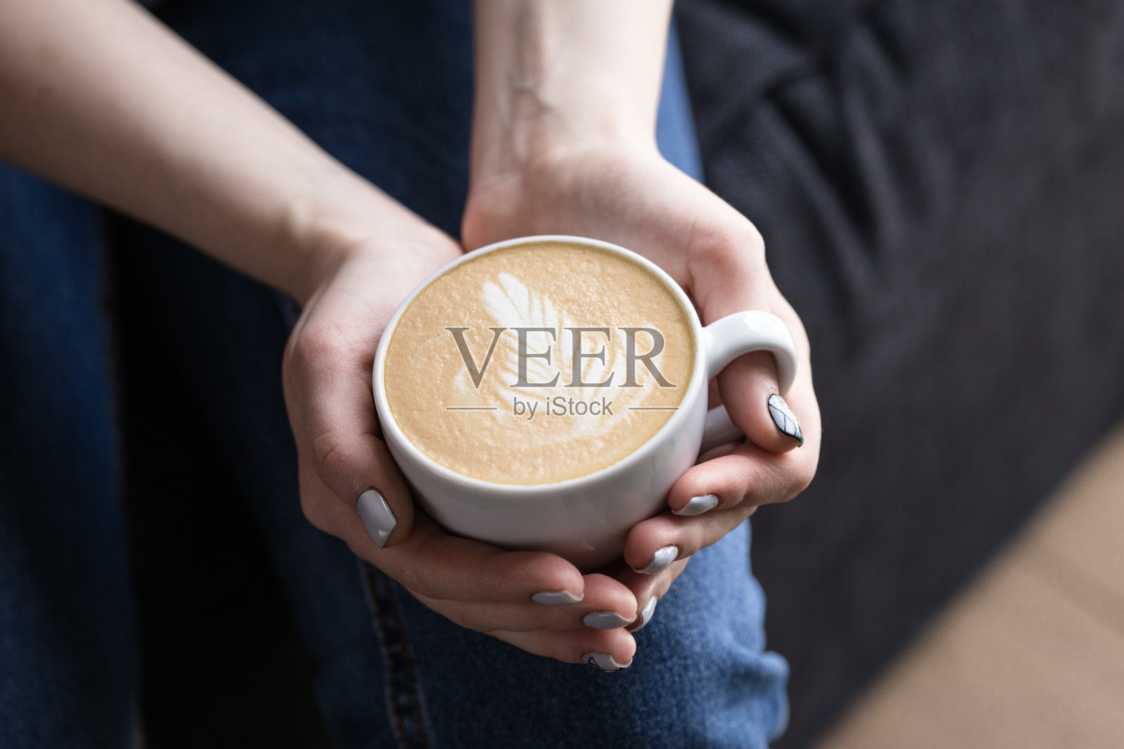 顶视图的热卡布奇诺咖啡在咖啡馆，心形奶油咖啡杯。手握热咖啡在杯子里的女人，女人闻和喝热咖啡的感觉很好在咖啡店照片摄影图片