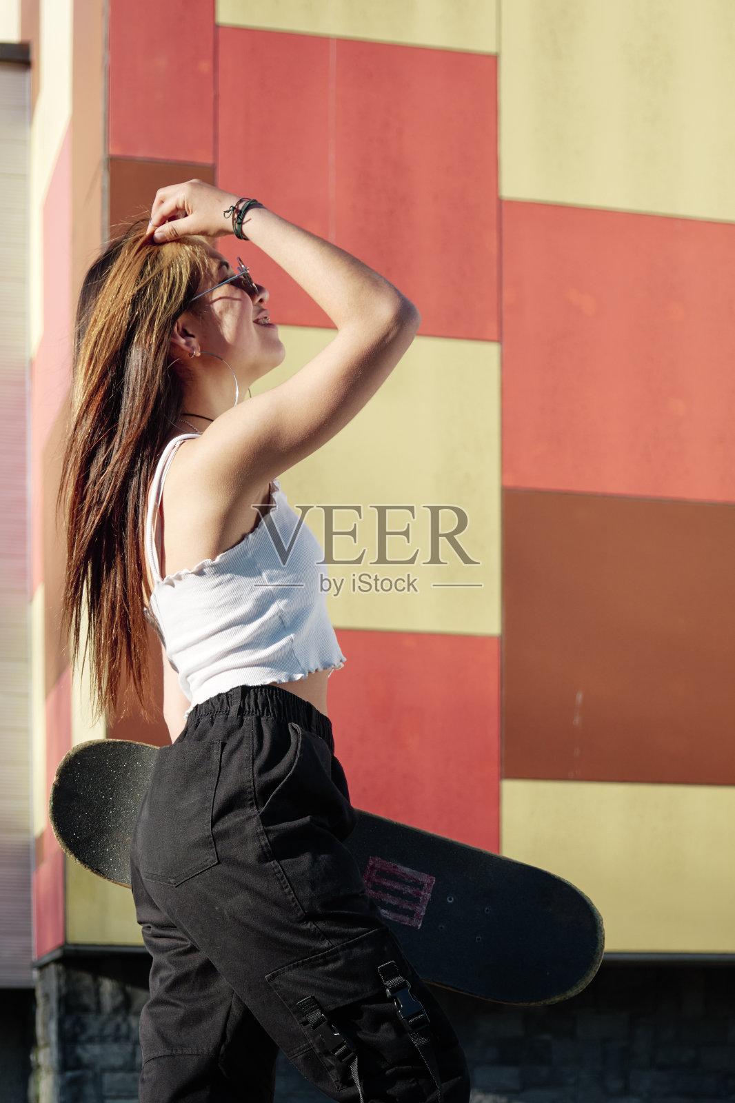 年轻的女孩抚摸着她的长发，拿着她的滑板照片摄影图片