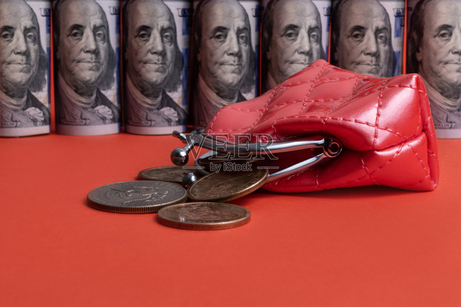 在卷起的100美元钞票的背景下，一个迷你红色钱包里涌出了美国硬币照片摄影图片