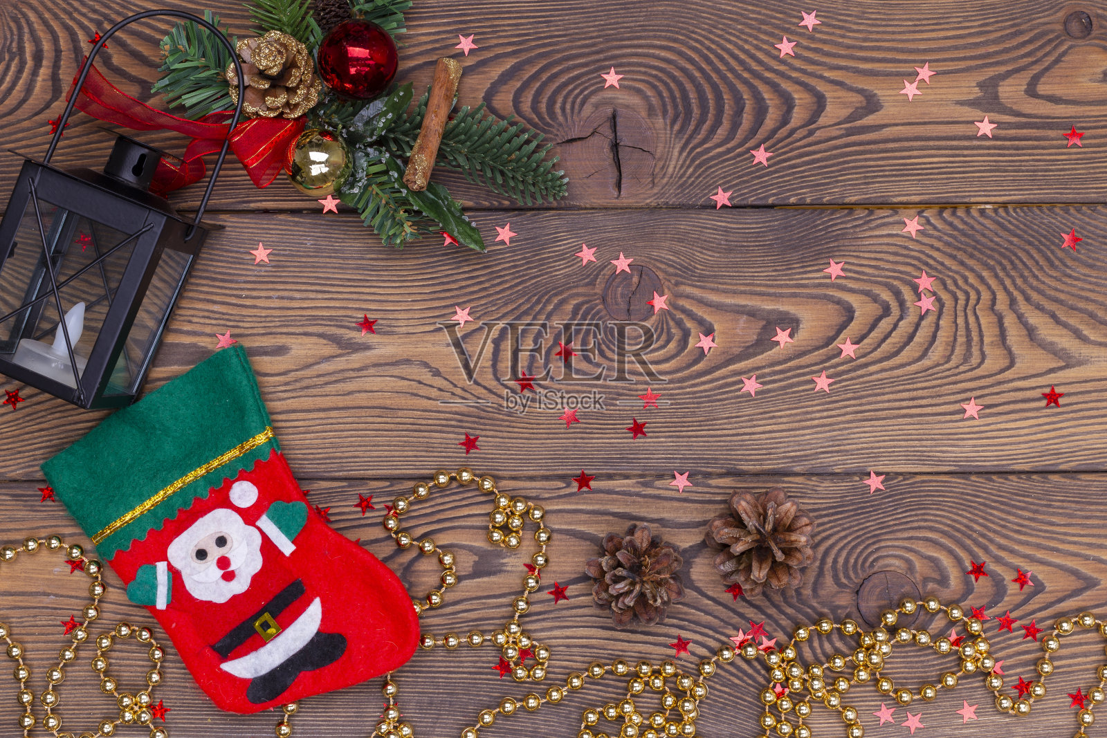 有圣诞老人形象的红色长筒袜和一个有圣诞装饰的黑色灯笼，木桌上有珠子。俯视图，复制空间照片摄影图片