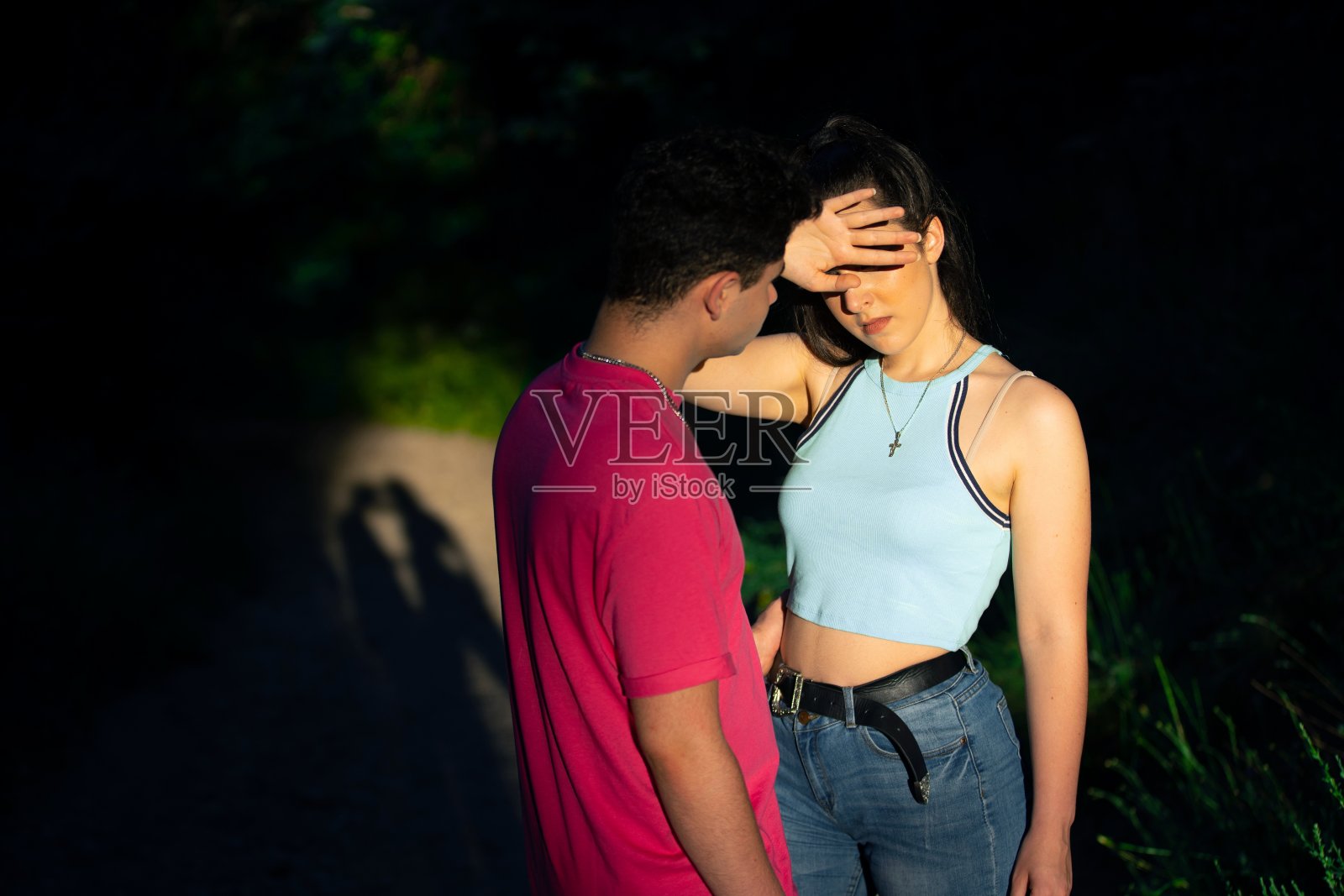 一个男孩和一个女孩被太阳照亮，女孩盖住她的脸，这样光就不会打扰她照片摄影图片