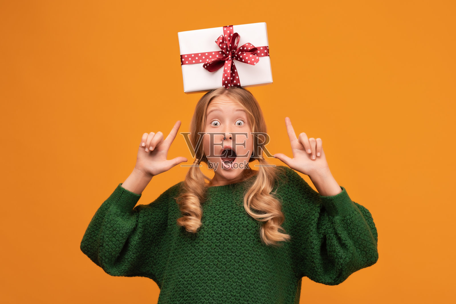 迷人的金发少年拿着礼盒在她的头上。工作室拍摄，黄色背景。新年生日假期概念照片摄影图片