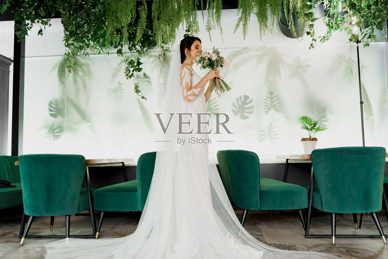 年轻迷人的新娘穿着婚纱婚纱看着花束和微笑。穿着婚纱的女孩在现代餐厅。为婚庆公司的社交网络做广告。照片摄影图片