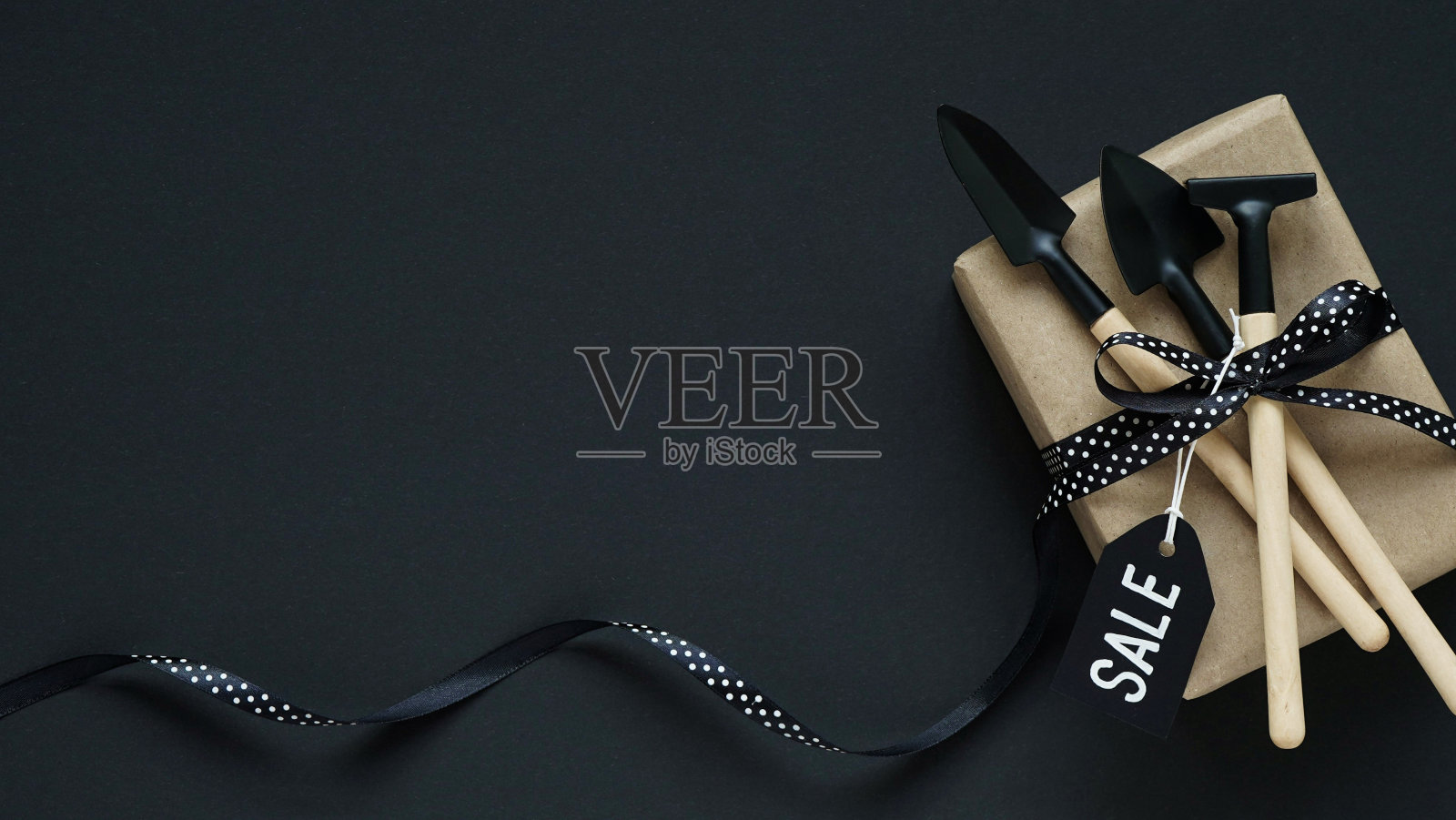 黑色星期五的网上购物。棕色礼盒，花园工具与黑色蝴蝶结在白色的豌豆和黑色的标签在黑色的背景，俯视图，平面lay，复制空间。园林工具销售理念。照片摄影图片