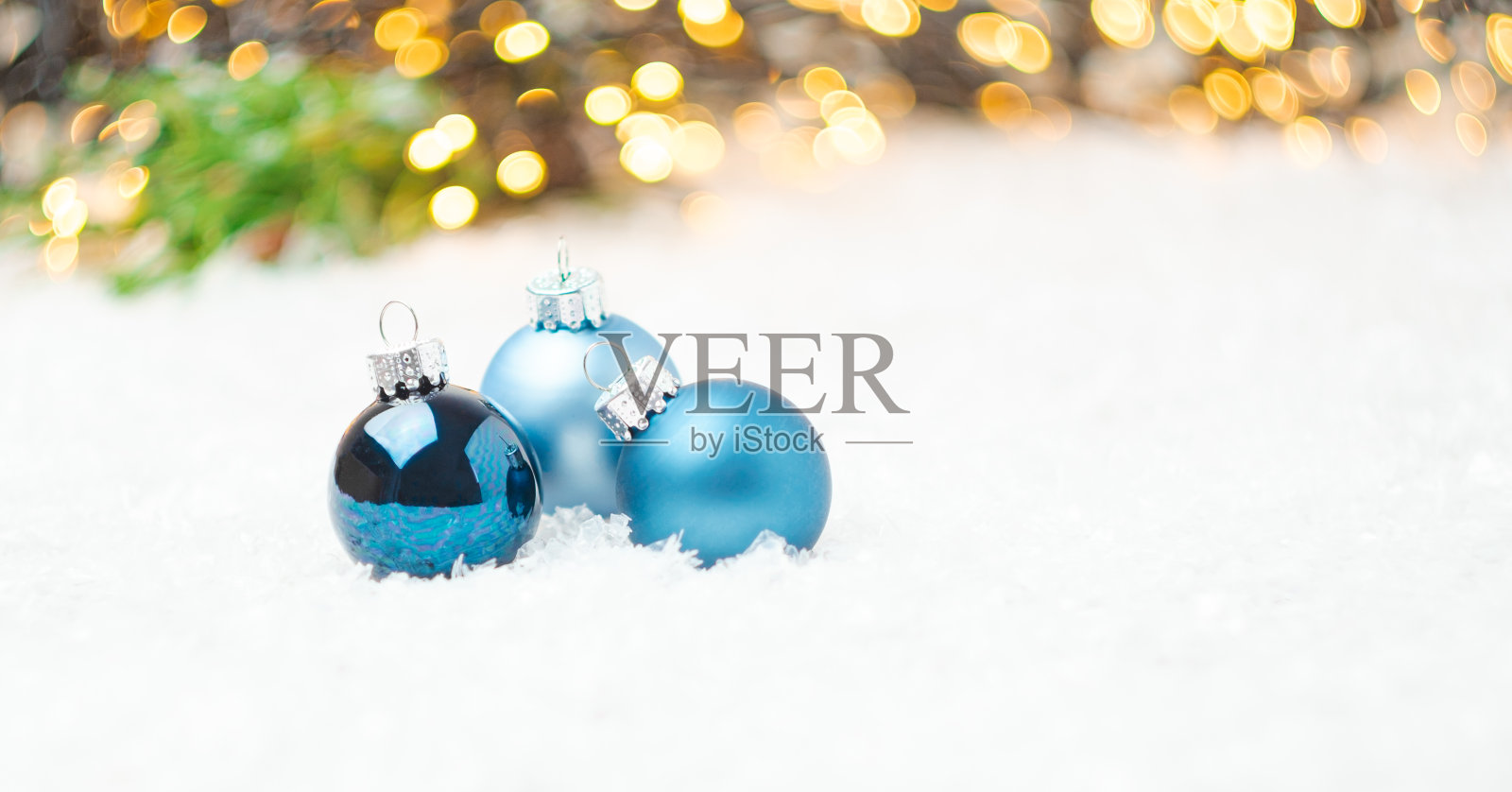 蓝色的圣诞球放置在圣诞树的背景上的雪和模糊的金色灯光与拷贝空间。准备新年晚会。照片摄影图片