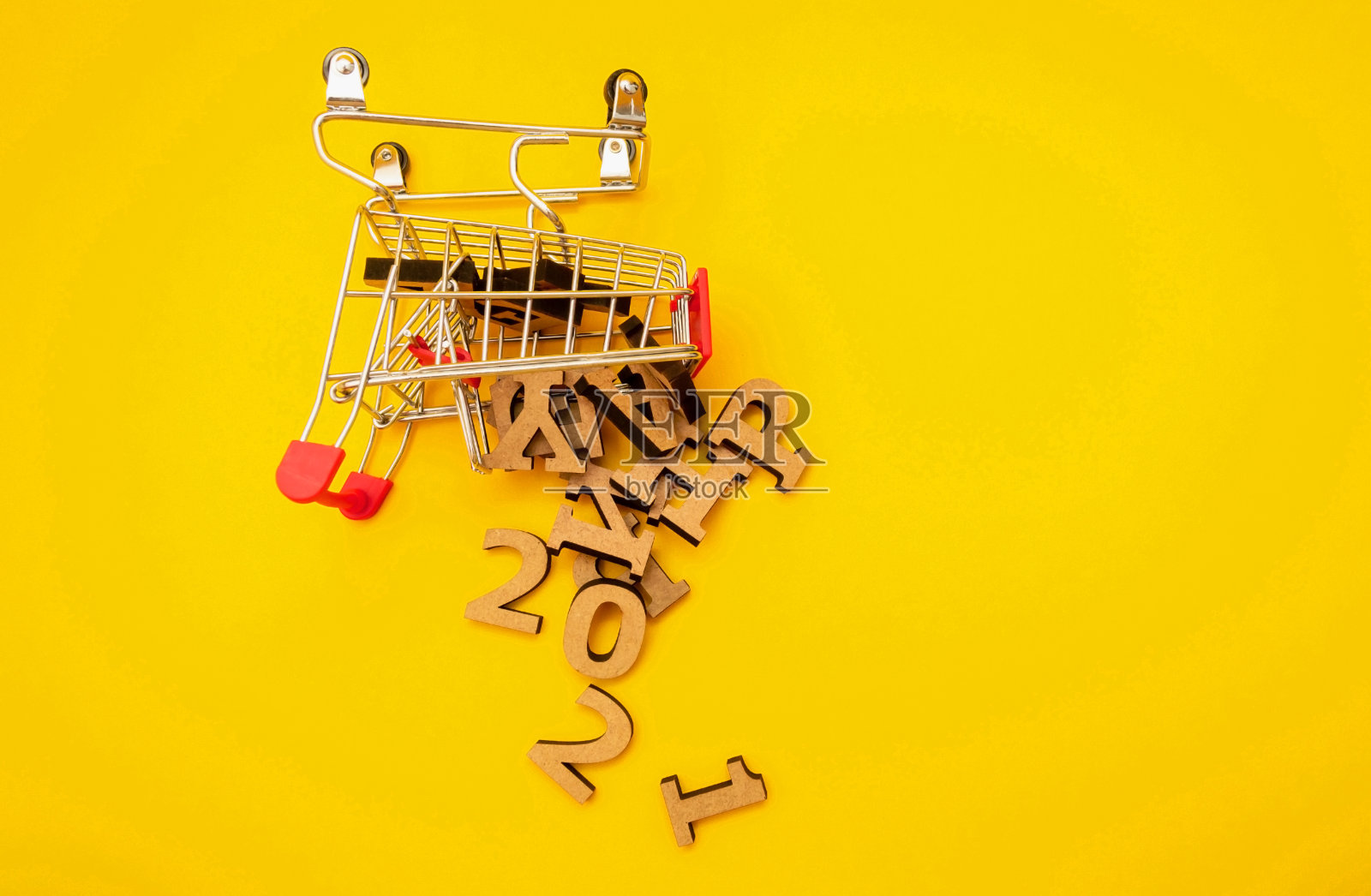 2021年新年快到了。木制的字母从一辆杂货店的购物车上掉落在黄色的背景上。节日装饰或明信片的概念。俯视图和平视图。本空间照片摄影图片