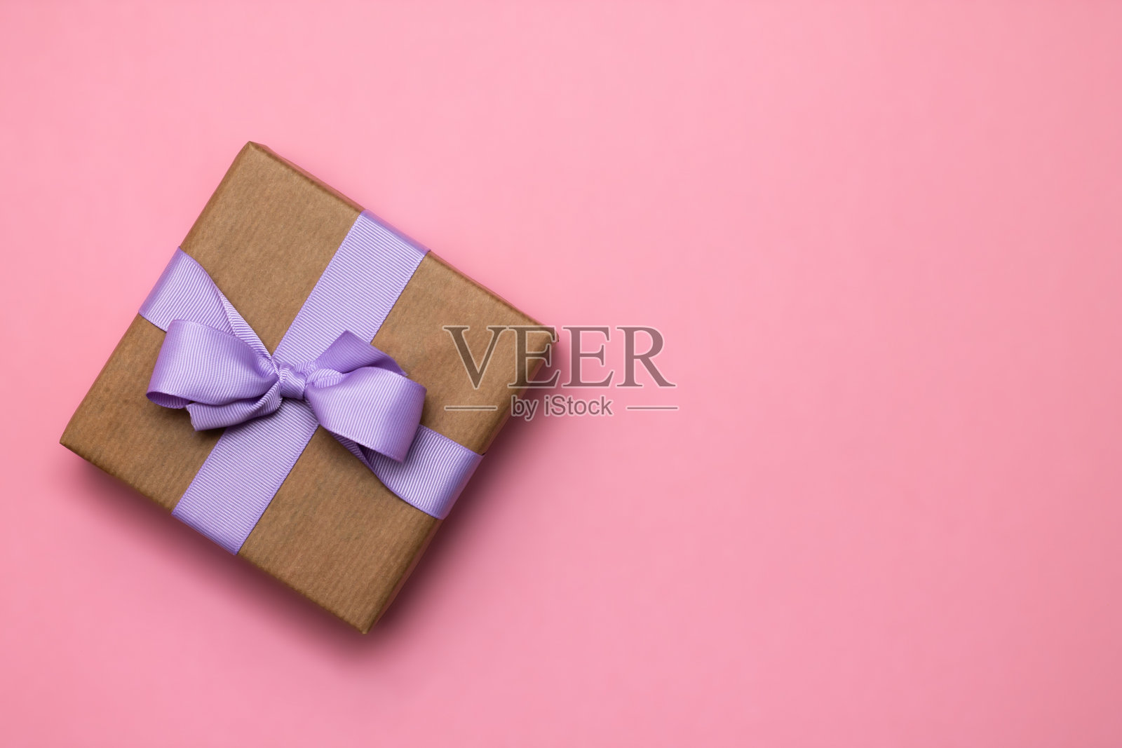 礼物在牛皮纸与淡紫色丝带在粉红色的背景。前视图。副本的空间。照片摄影图片