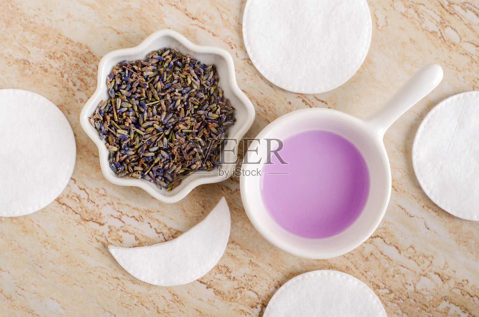 小白碗，里面有自制的芳香紫色调色剂、干薰衣草花和棉垫。天然化妆品成分。有机护肤，自制化妆品和水疗概念。平躺照片摄影图片