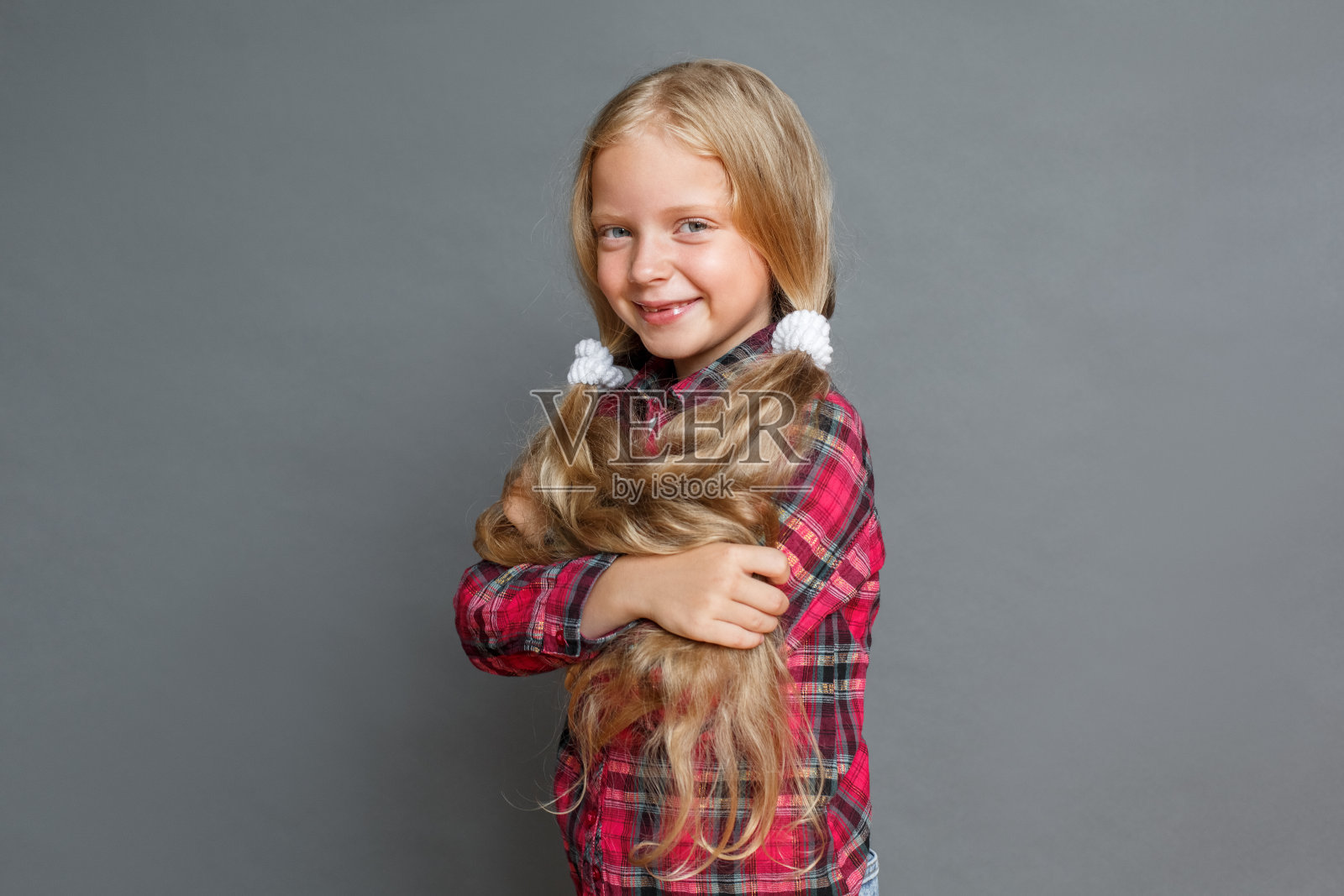 扎着马尾辫的小女孩孤立地站在灰色的怀抱里，看起来很开心照片摄影图片