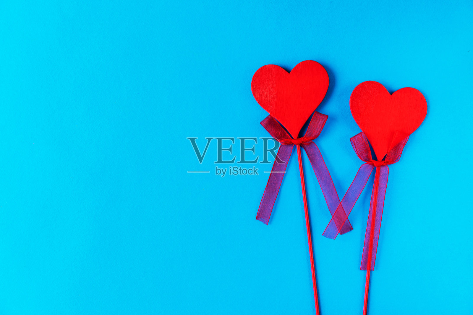 蓝色背景上的蝴蝶结，木棍上的两颗红色木心。这里有文本的位置。它可以在计算机桌面或手机屏幕保护程序上。或者像一张明信片照片摄影图片