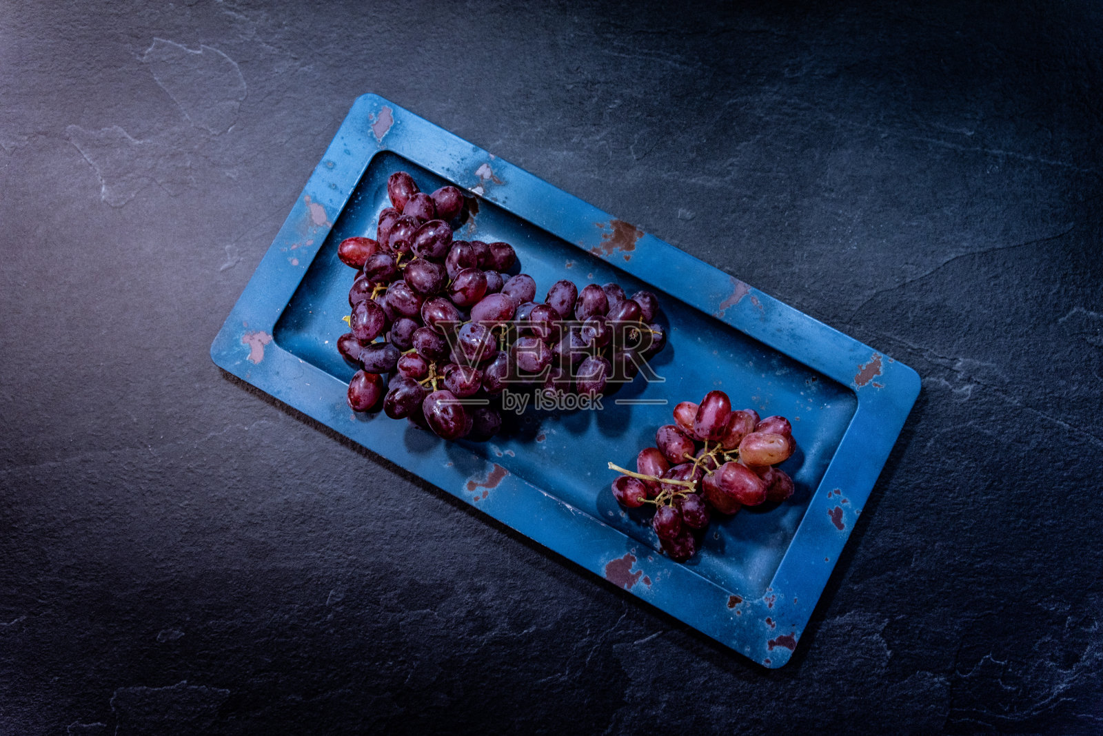 蓝色盘子上的葡萄放在有纹理的背景上照片摄影图片