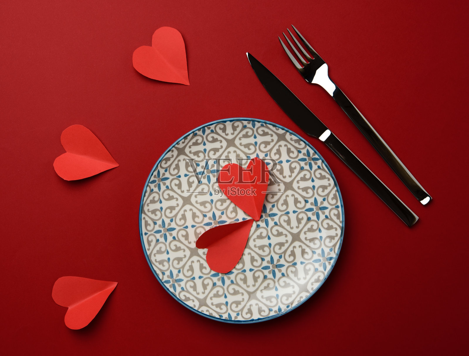 红色的纸心放在一个白色的圆形陶瓷板上照片摄影图片