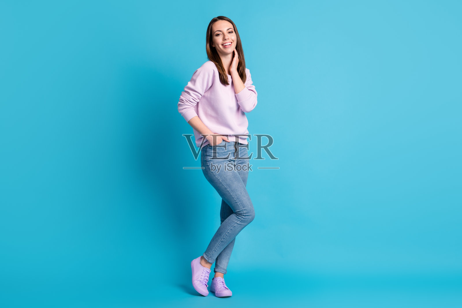 全身照片漂亮迷人的女士好心情触摸脖子梦想家喜气洋洋的微笑街道看穿休闲的紫色运动衫套头衫鞋子牛仔裤孤立的蓝色背景照片摄影图片