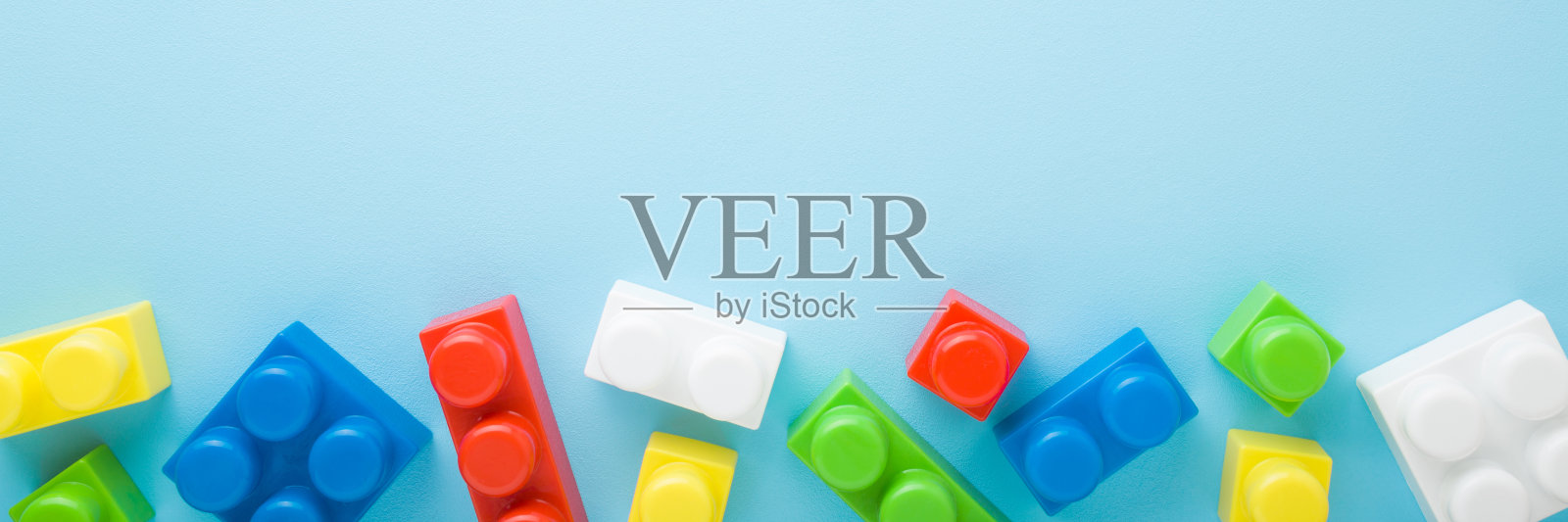 色彩鲜艳的塑料块在浅蓝色的桌子背景。柔和的颜色。特写镜头。给小孩子的发展玩具。文本的空位置。宽横幅。自顶向下的观点。照片摄影图片