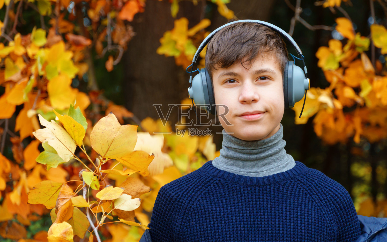 一个青少年的肖像听音乐耳机，放松在秋天的城市公园，明亮的黄色枫叶为背景照片摄影图片