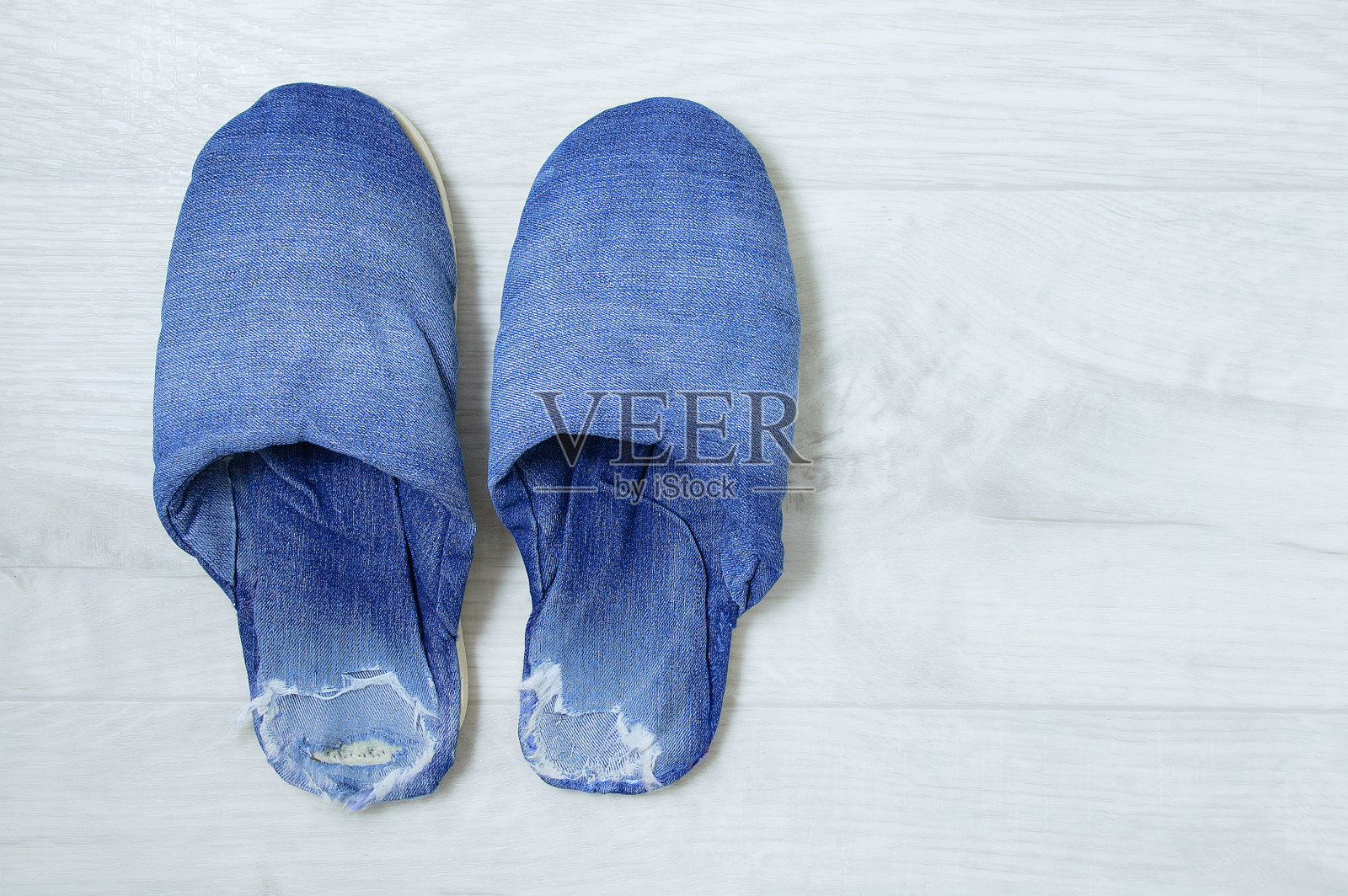 破旧的破洞牛仔鞋，灰色木制背景。照片摄影图片