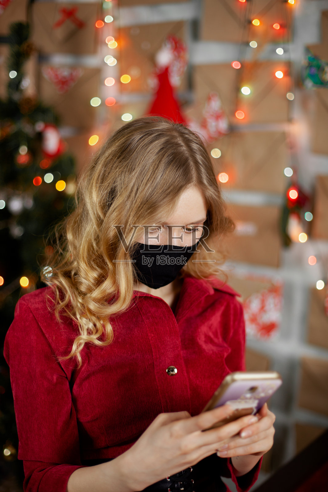 一个戴着医用口罩的美丽女孩的肖像，站在家里装饰好的圣诞树前照片摄影图片