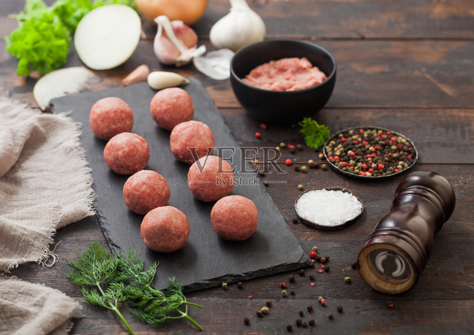 生牛肉丸子放在石板上，肉末放在碗盘中，配以胡椒、盐和大蒜，背景颜色较深，配以欧芹。照片摄影图片