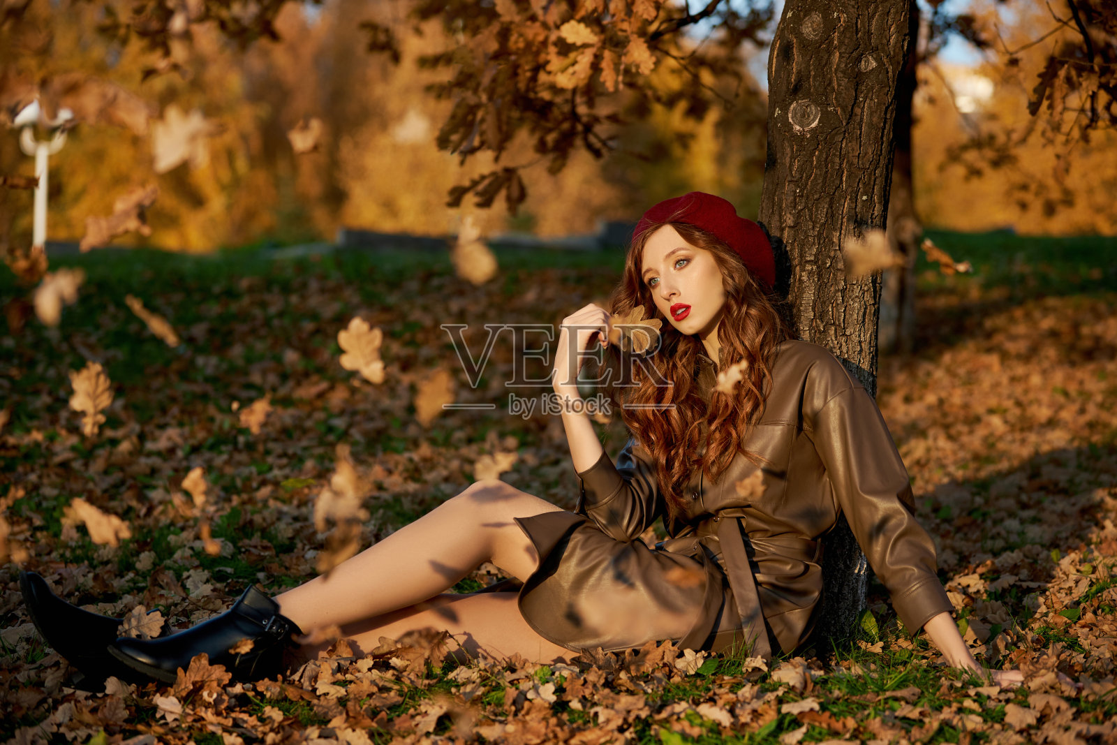 一个女人在秋天的肖像帽子贝雷帽和雨衣附近的一棵树在秋天黄色的树叶照片摄影图片