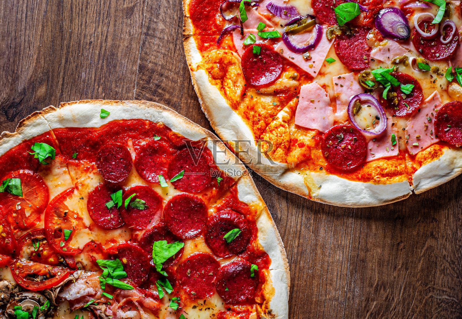 意大利辣香肠披萨和四季披萨配马苏里拉芝士，火腿，番茄酱，意大利腊肠，培根，蘑菇，胡椒，香料和新鲜罗勒。木桌背景上放着两个意大利披萨照片摄影图片