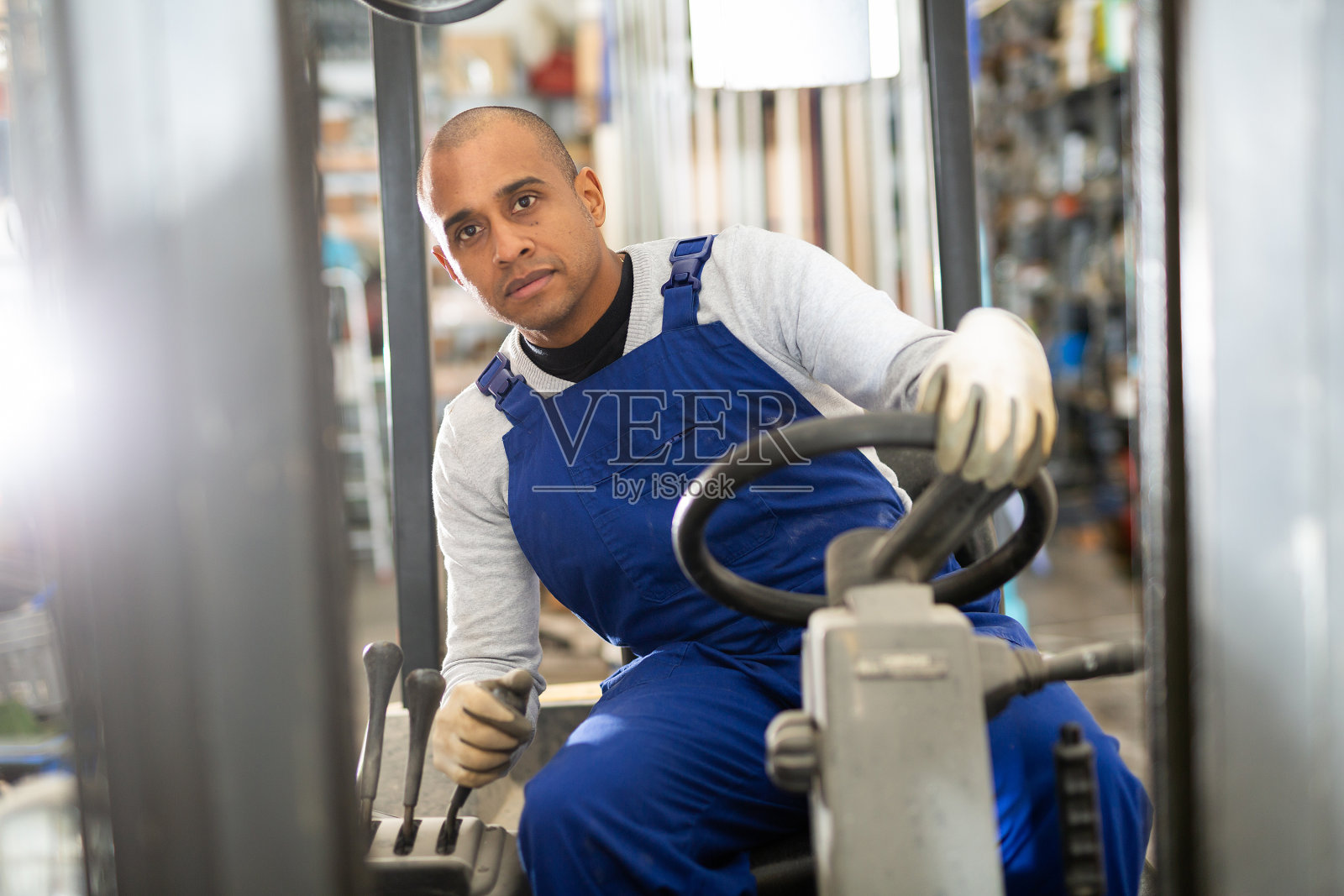 自信的西班牙裔工人在建材仓库驾驶叉车照片摄影图片