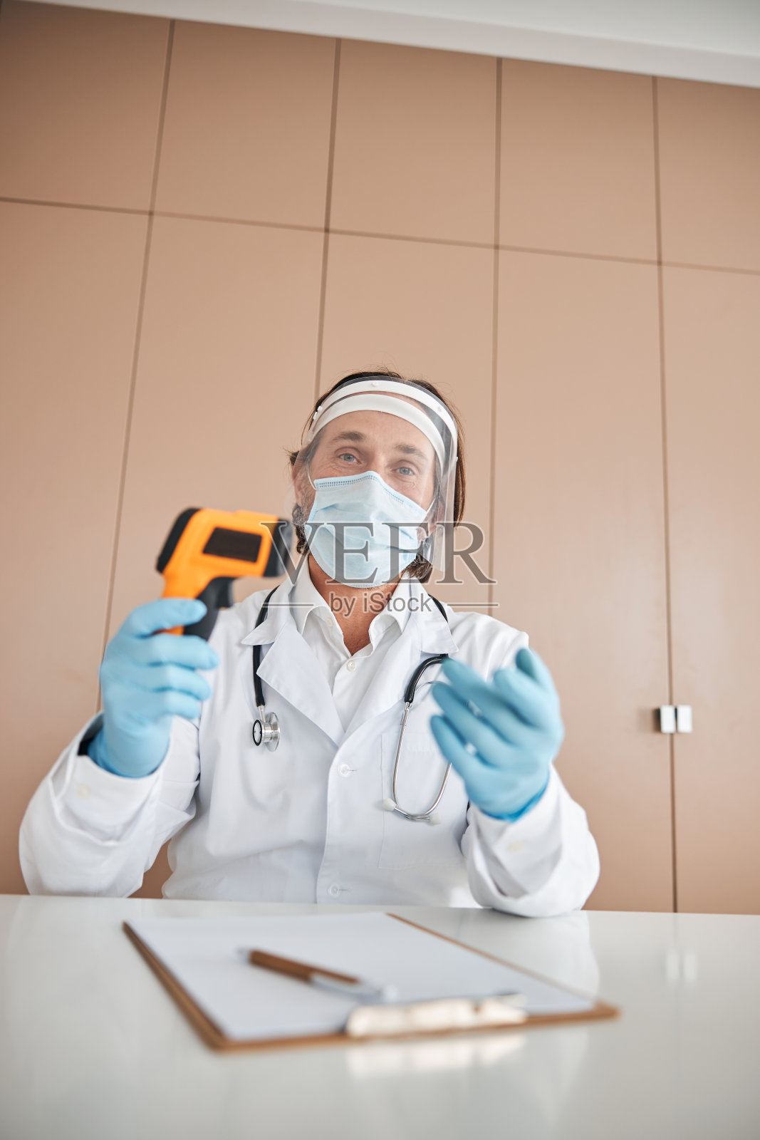 戴着面罩，穿着实验服，戴着非接触式温度计的人照片摄影图片