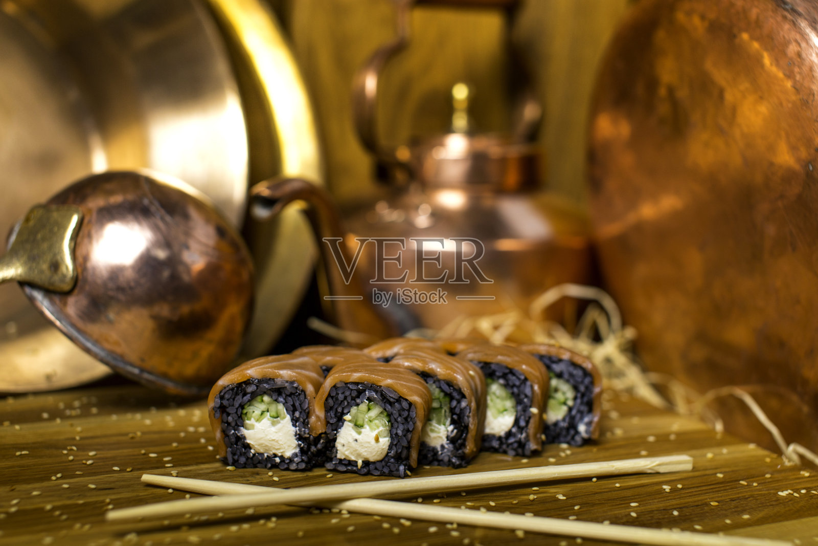 黑米费城寿司卷，上面有生鲑鱼片和芝麻，背景是铜餐具。静物画照片摄影图片