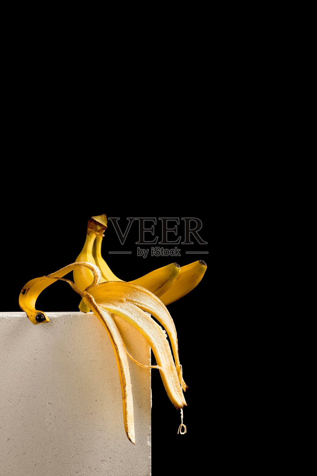 一只香蕉和香蕉皮放在白色的架子上，黑色的背景。海报概念或构思照片摄影图片
