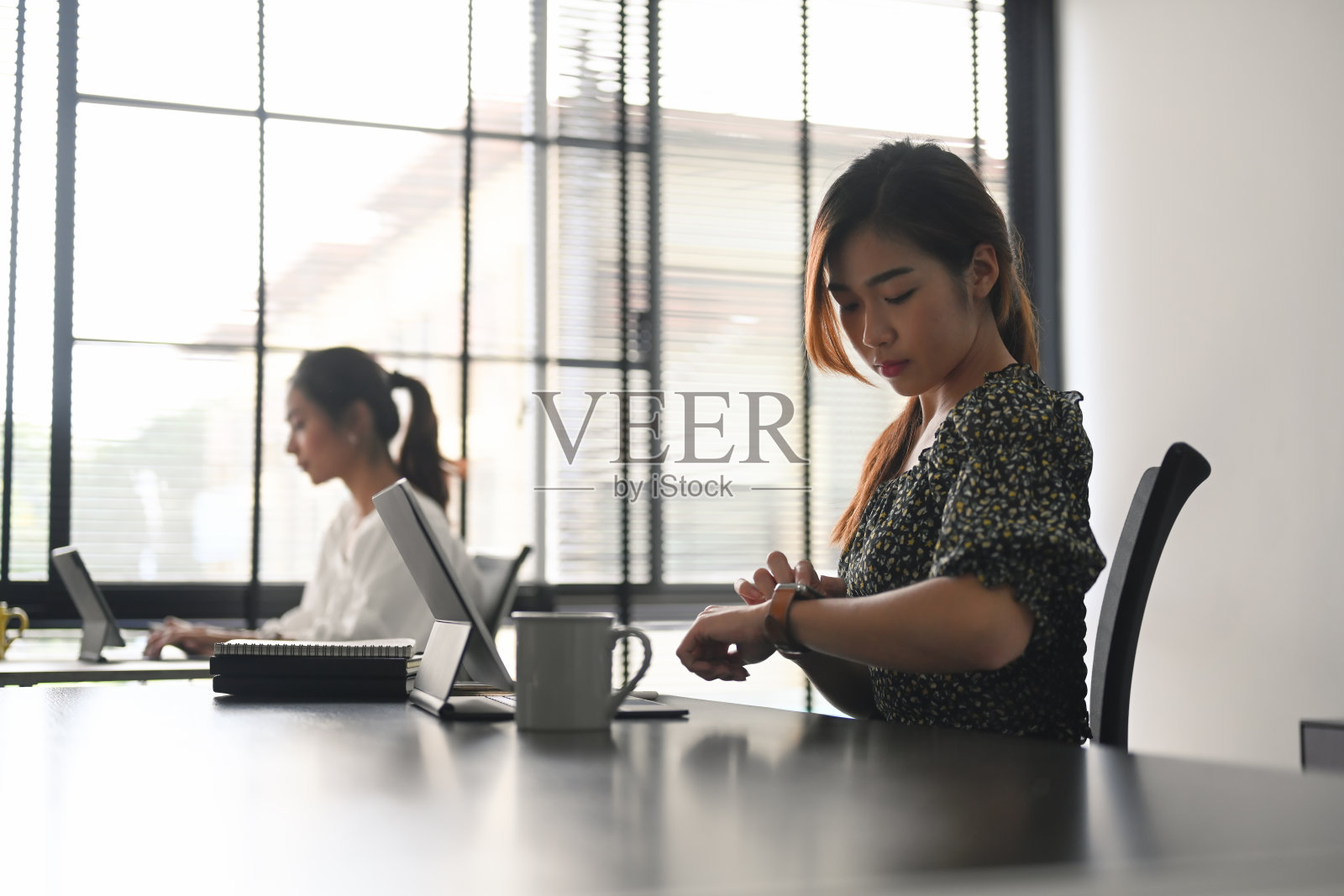 两个穿着休闲的女商人坐在一张桌子前，在一个现代化的办公室里用平板电脑工作。照片摄影图片